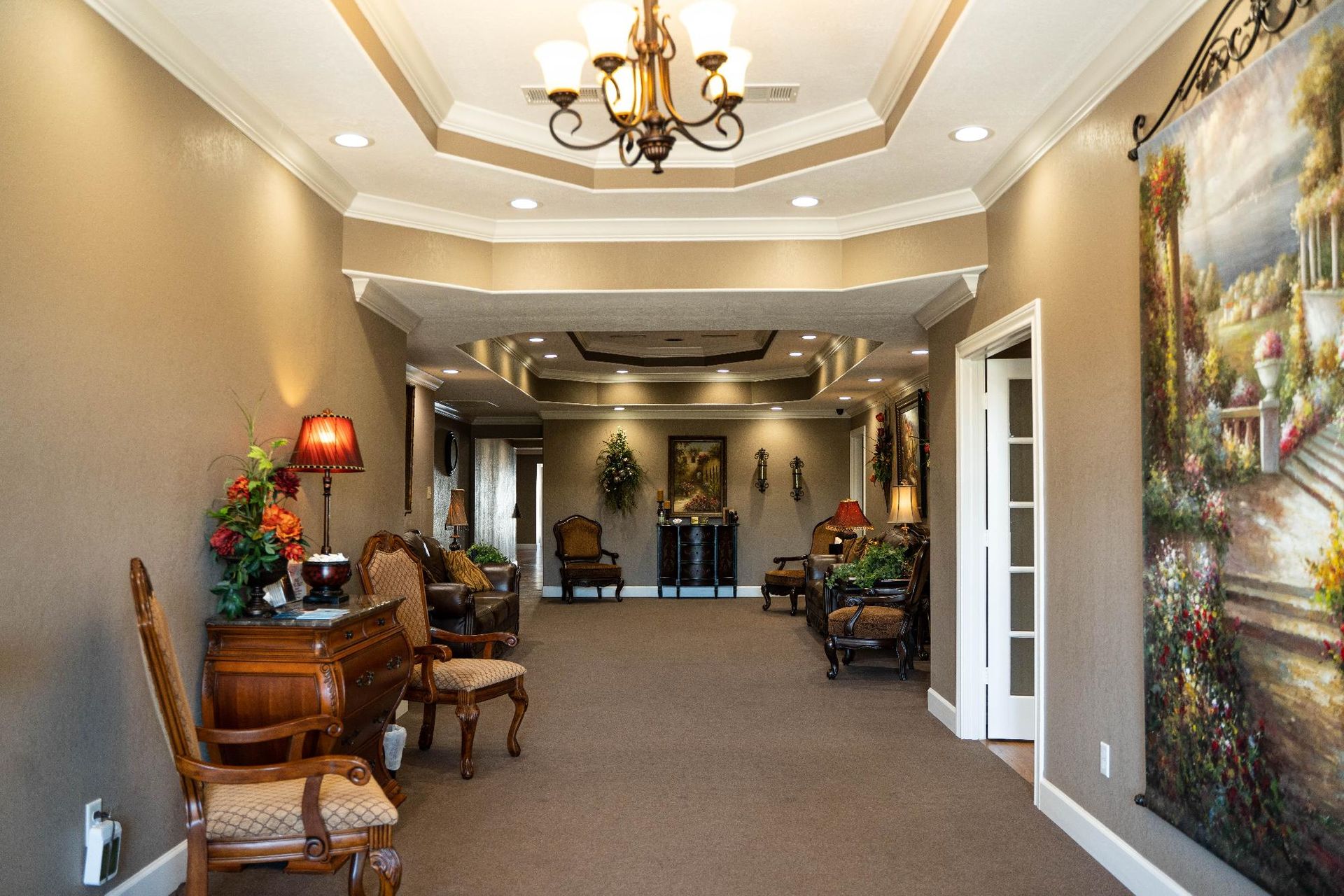 Elegant hallway with chandelier, chairs, table lamps, and a large wall mural.
