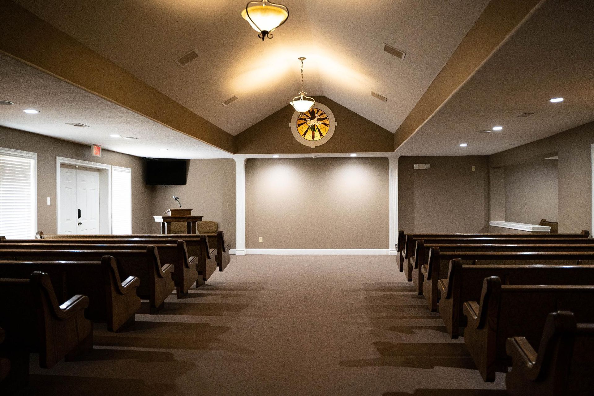 Empty church sanctuary with pews, carpeted aisle, and a large cross at the front