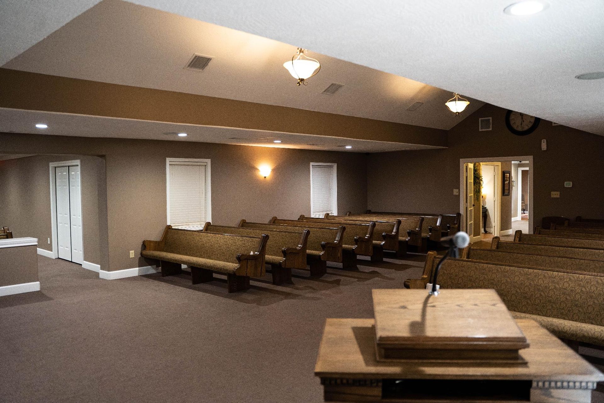 Church sanctuary with rows of brown pews, a pulpit, and a sloped ceiling with wall lights