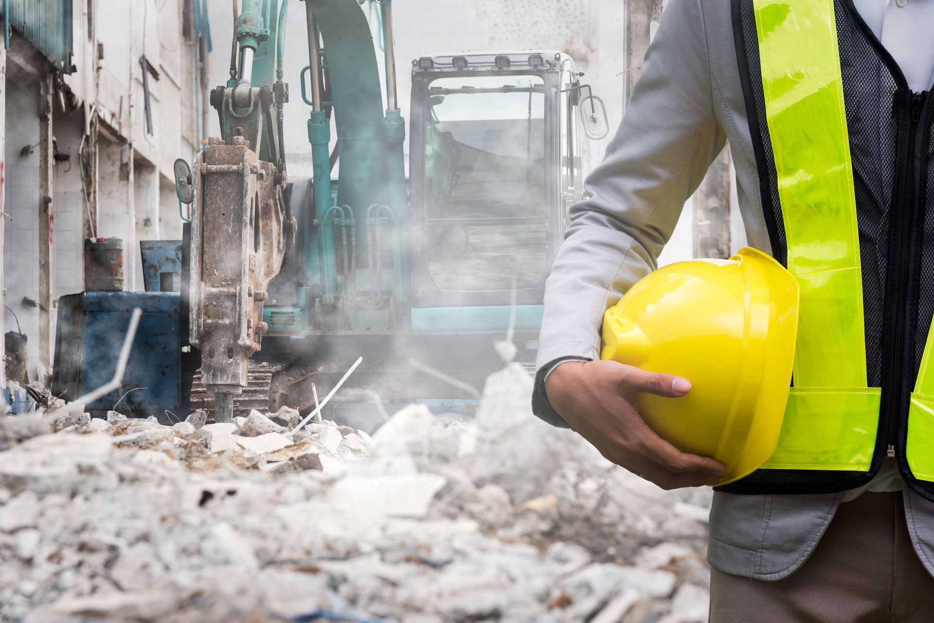 Construction worker holding a yellow hard hat at a demolition site with rubble and machinery