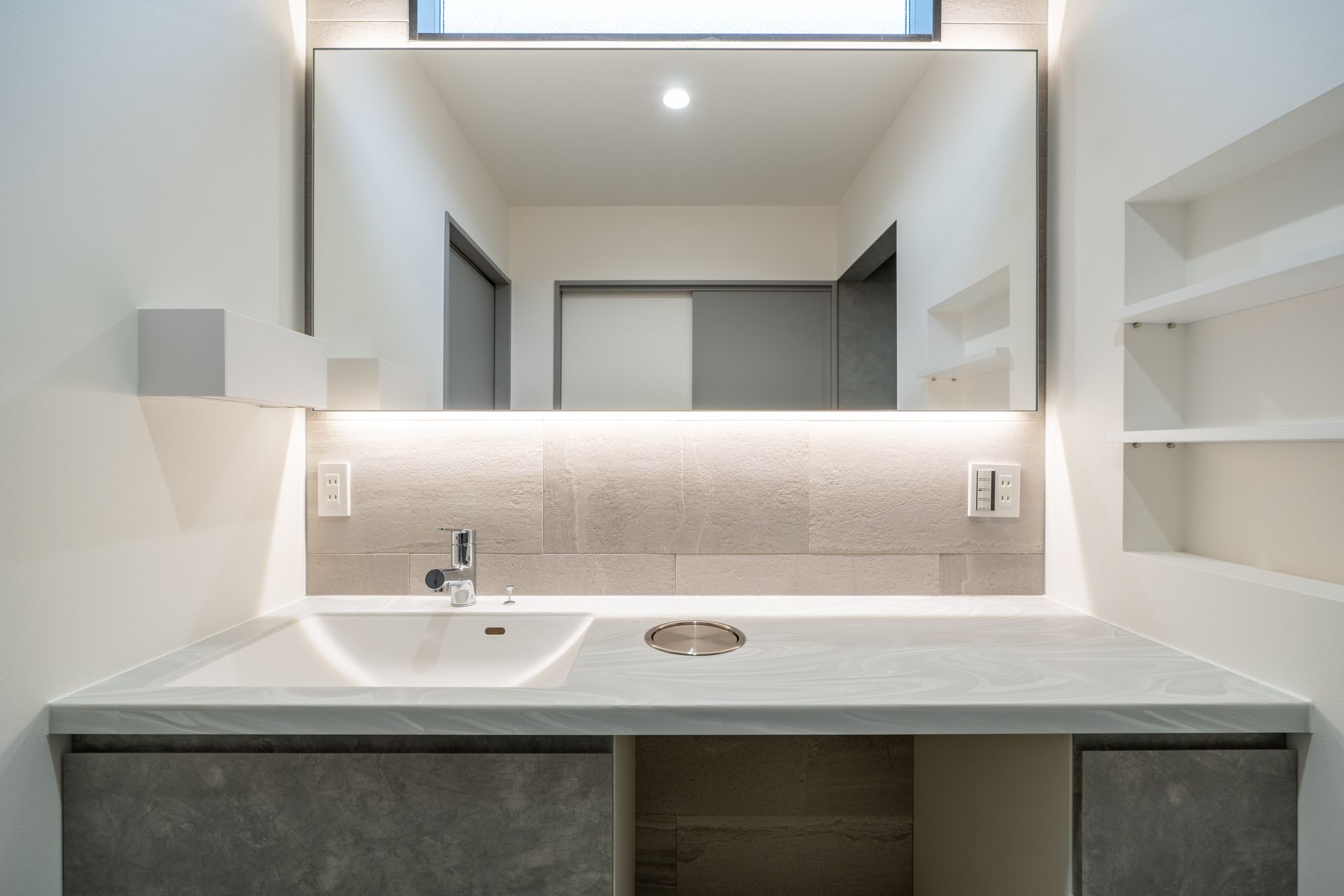 Modern bathroom vanity with large mirror, white sink, gray countertop, and built-in shelves