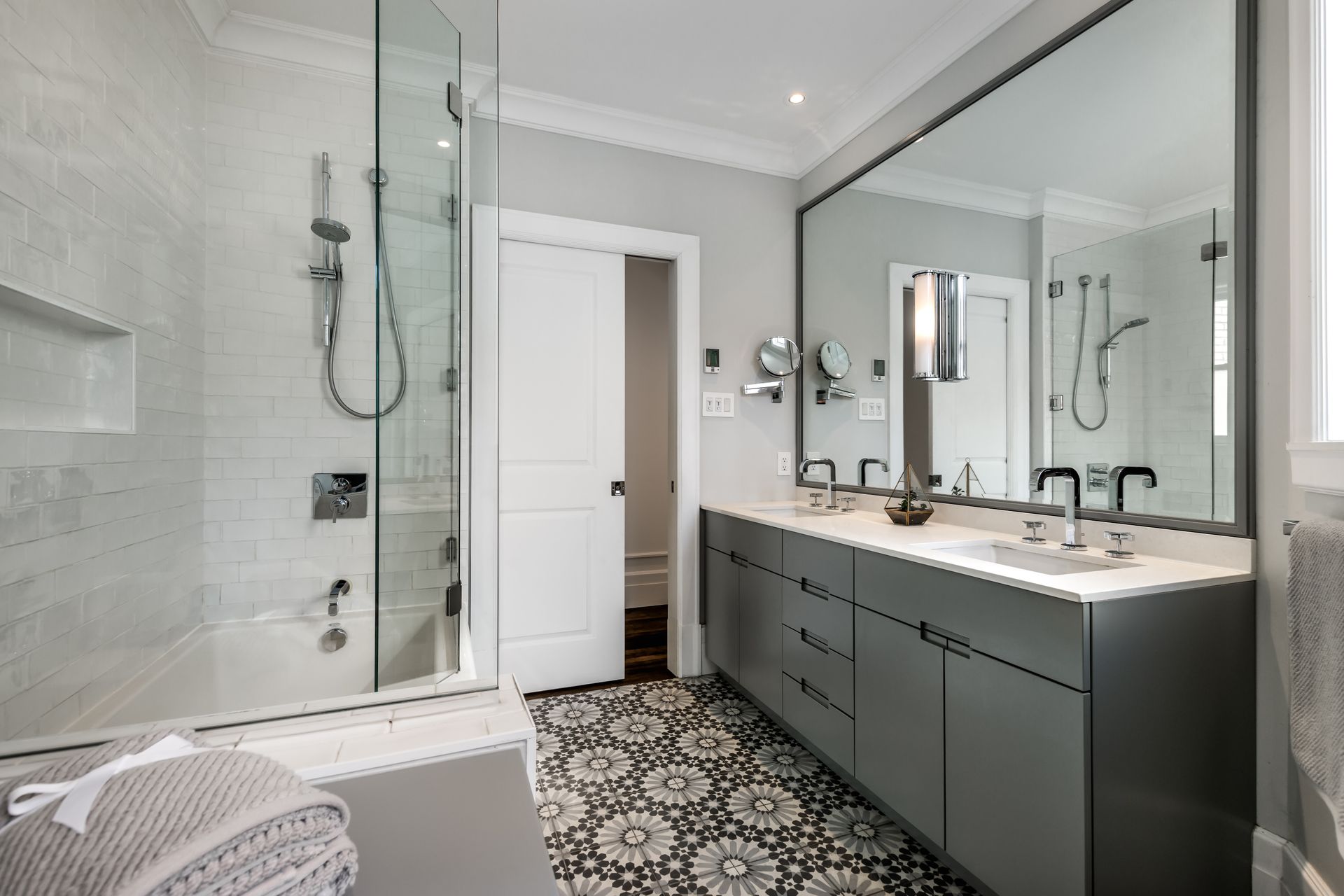 Modern bathroom with glass shower, large vanity mirror, and patterned black-and-white tile floor