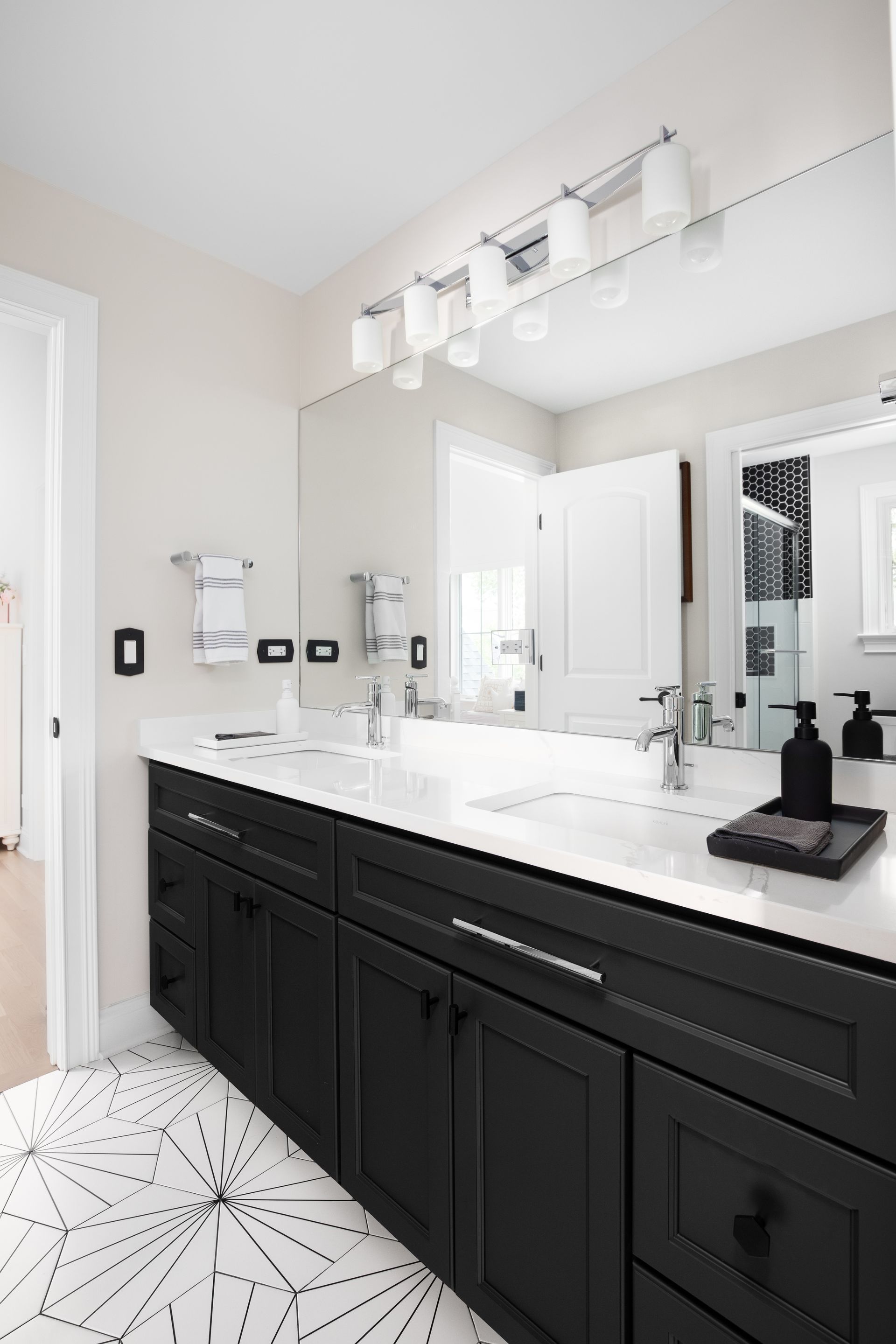 Modern bathroom with black vanity, white countertop, large mirror, and hexagon tile floor
