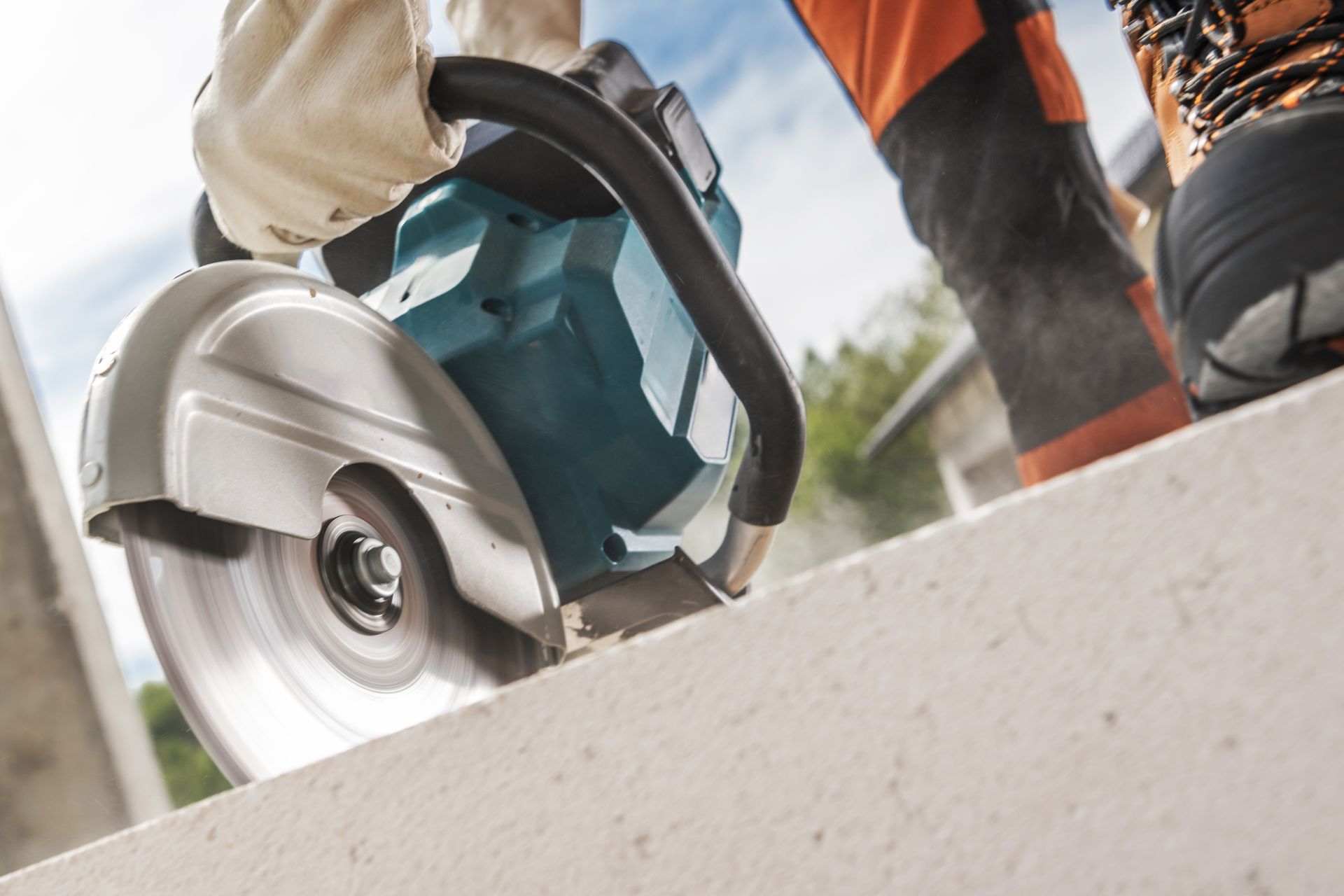 Worker using a teal circular saw to cut concrete on a job site
