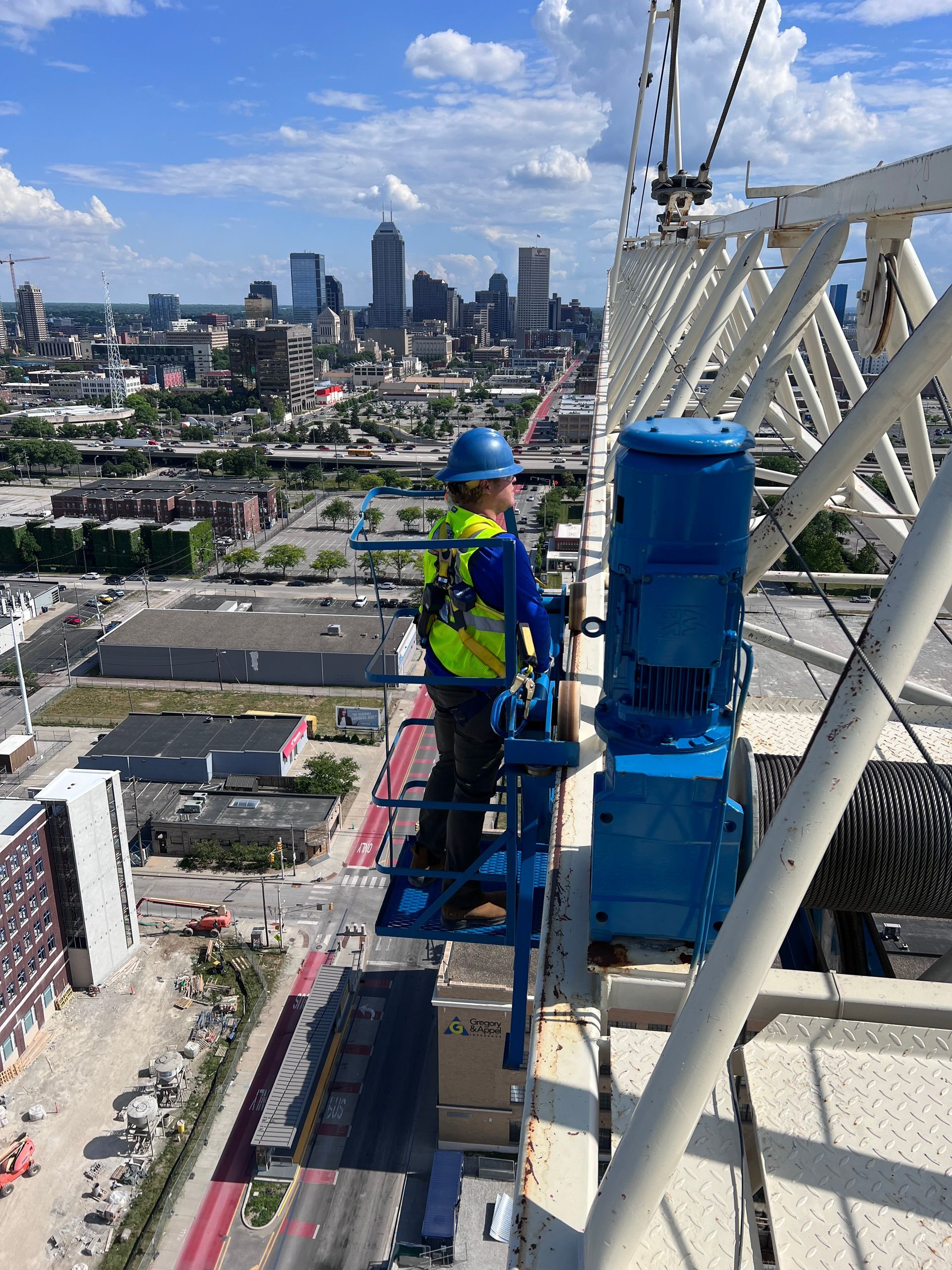 A man is standing on top of a crane with a city in the background.