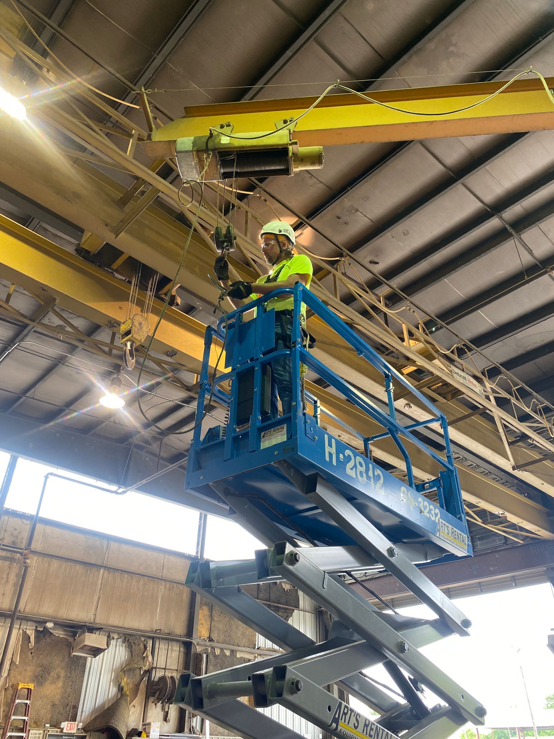 A man is standing on a scissor lift in a warehouse.
