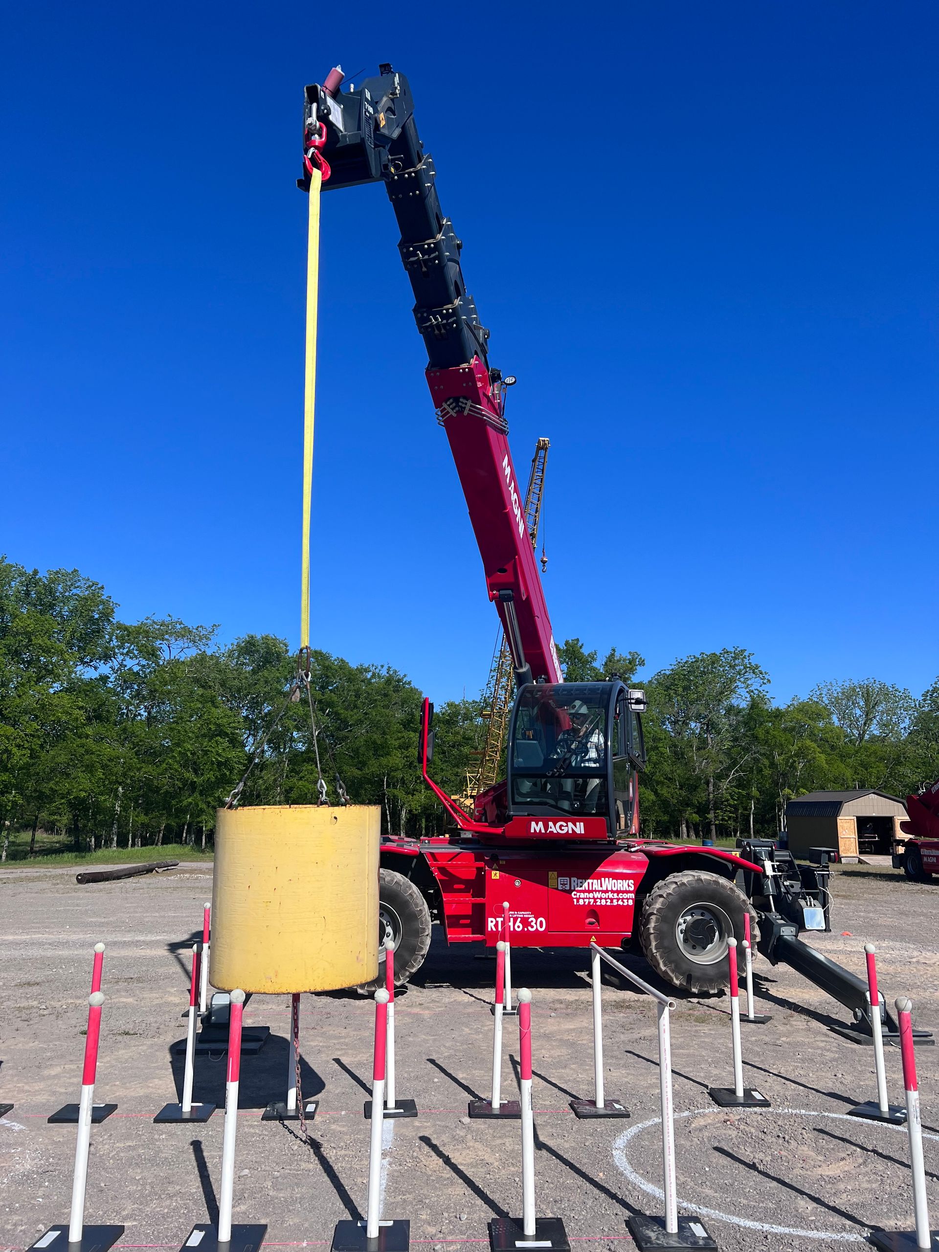 A red crane is lifting a yellow object in a parking lot.