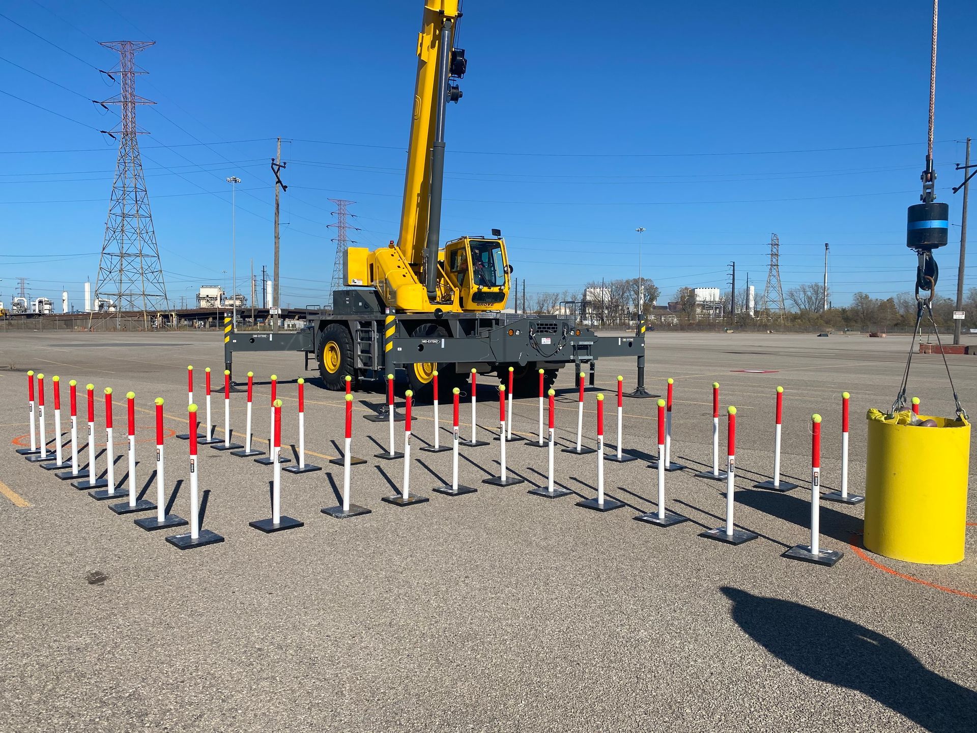 A yellow crane is sitting in a parking lot next to a row of red and white poles.
