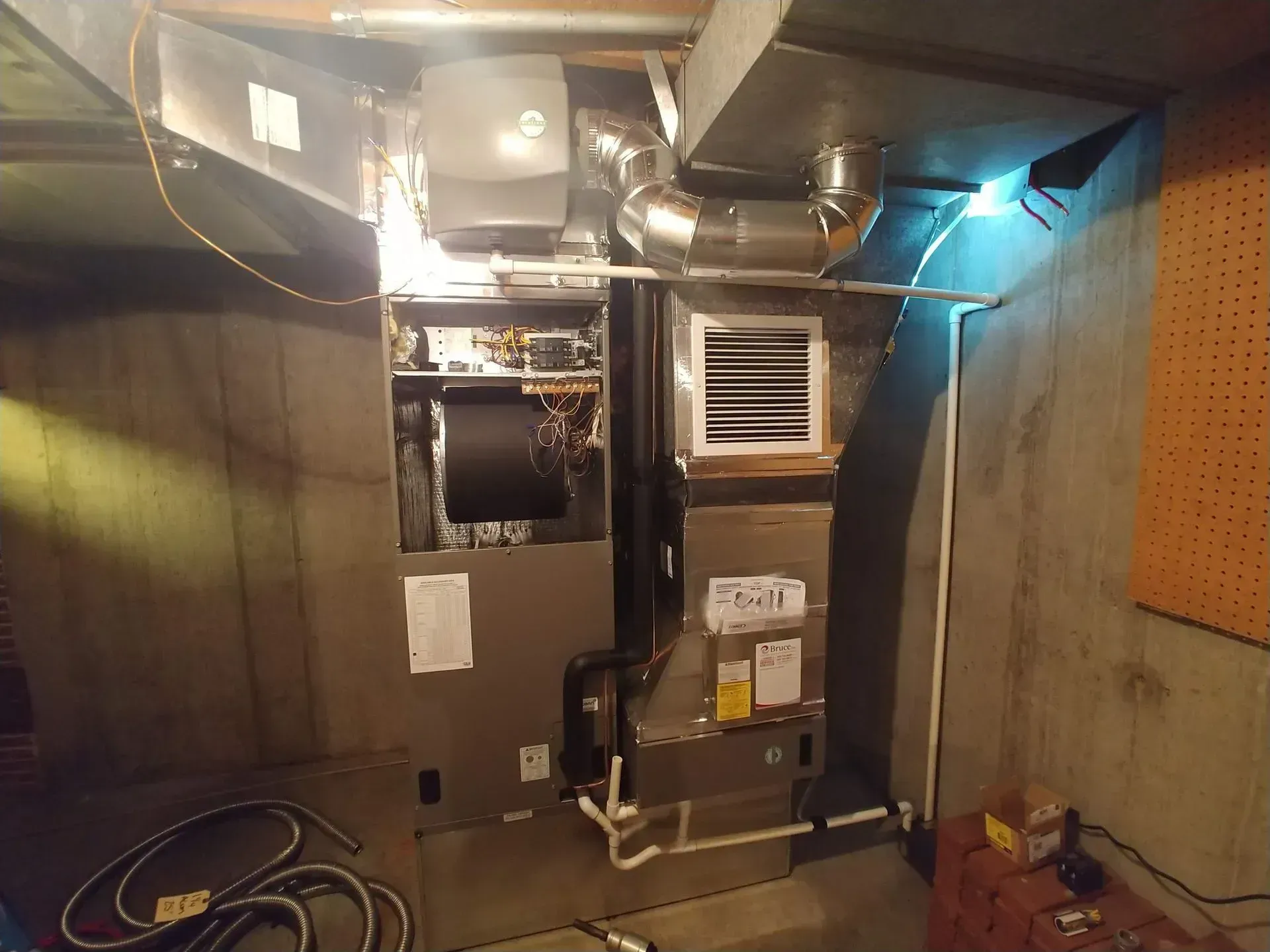 Furnace and air conditioning unit installed in a basement, with ductwork and wiring visible.