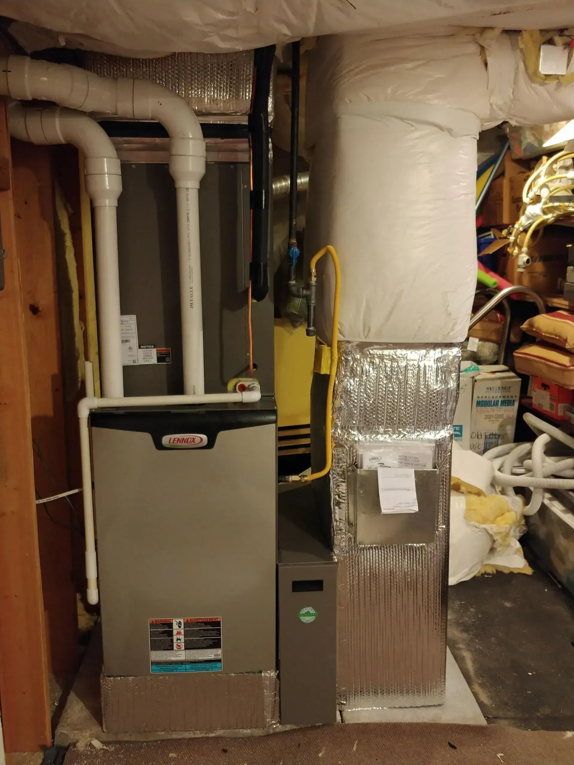 Furnace unit with ductwork and a white filter in a basement setting. Gray and white colors.
