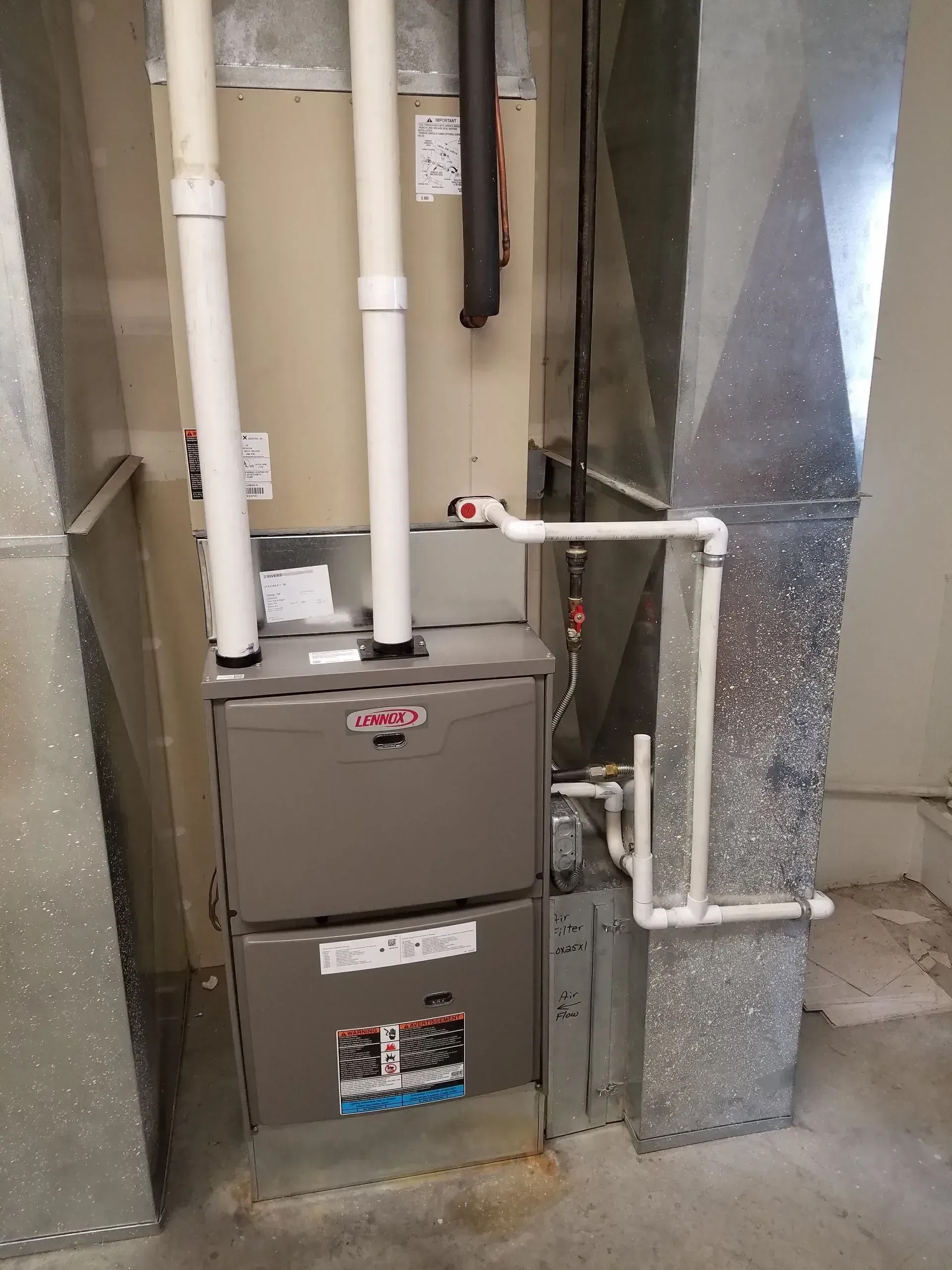 Lennox furnace with connected ductwork and PVC pipes in a utility room. Gray and white.