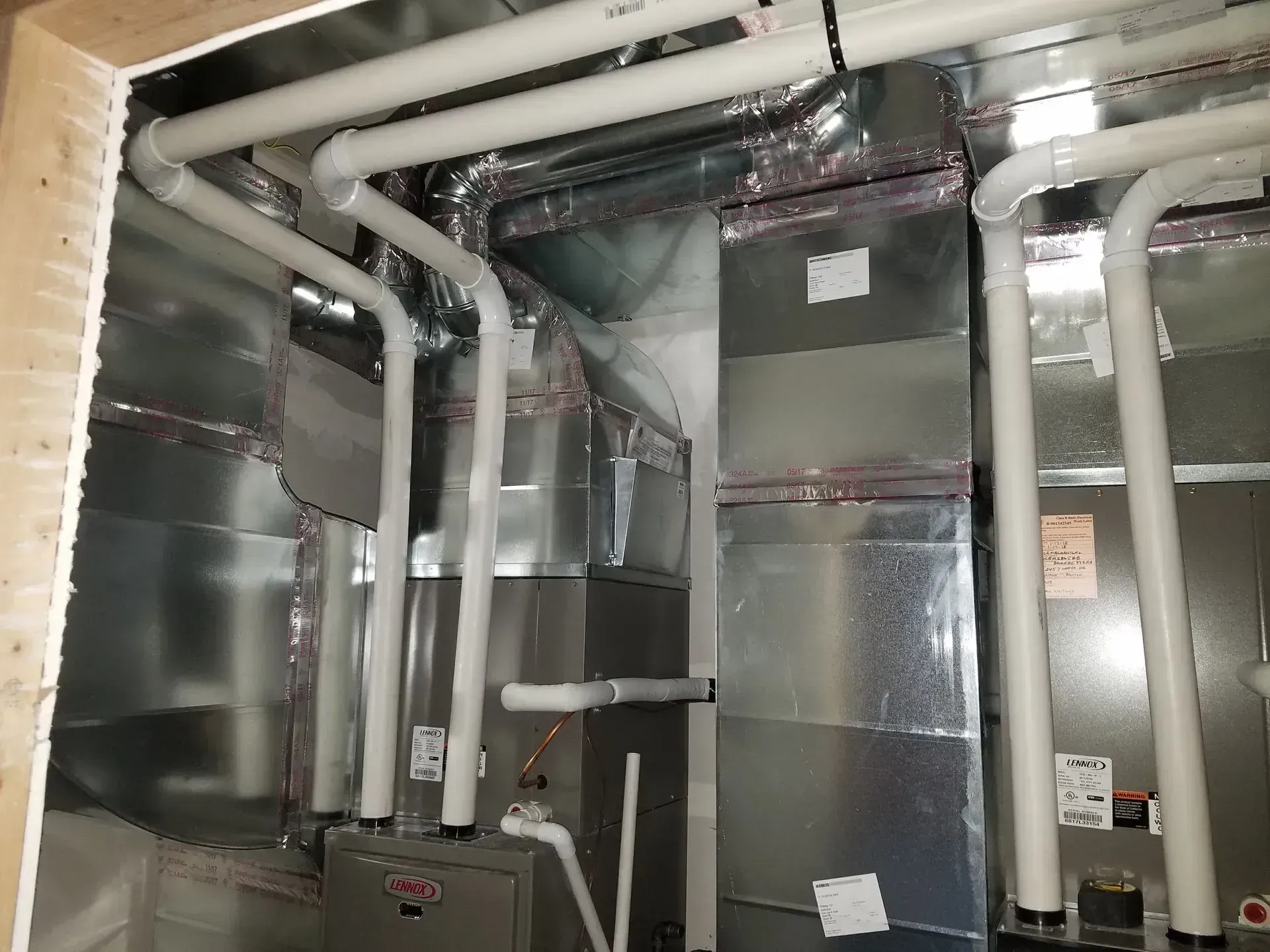 Interior view of an HVAC system with metallic ducts and white PVC pipes in an enclosed space.