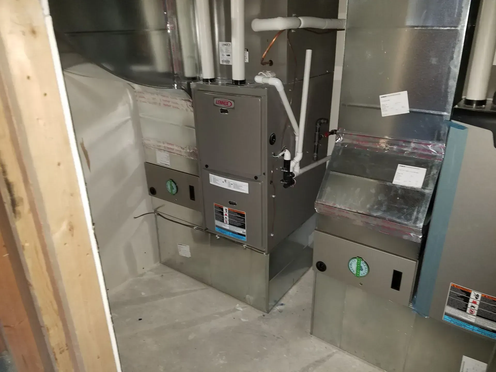 Furnace and ductwork in a basement setting; silver metal and white pipes against gray walls.
