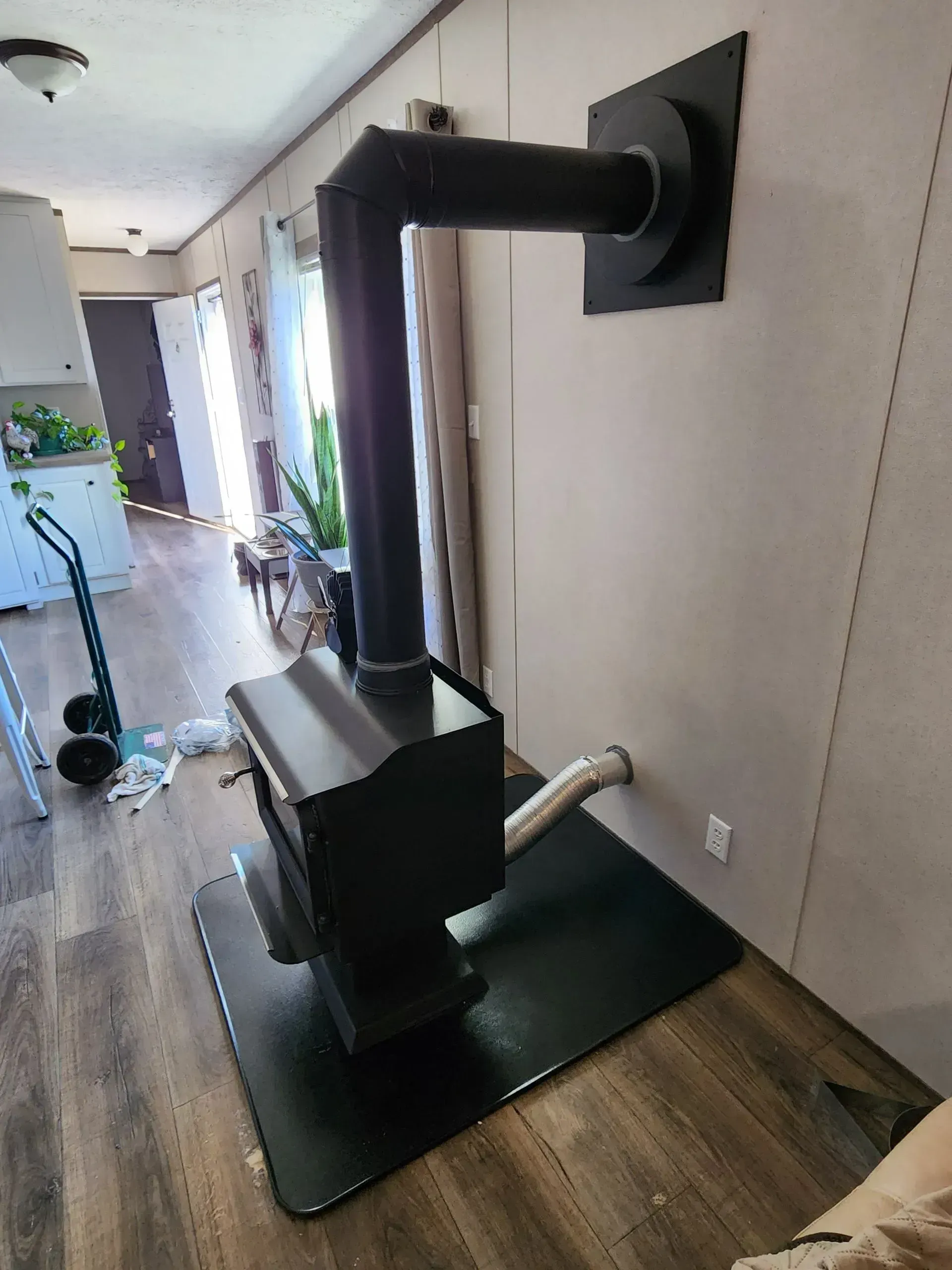 Black wood-burning stove with black pipe installed on a wall in a room with wood flooring.