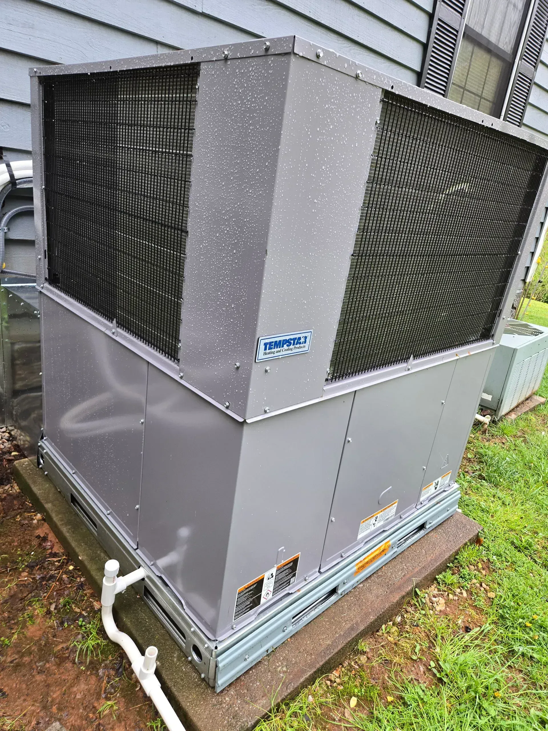 Gray HVAC unit on a concrete pad next to a building, surrounded by grass.