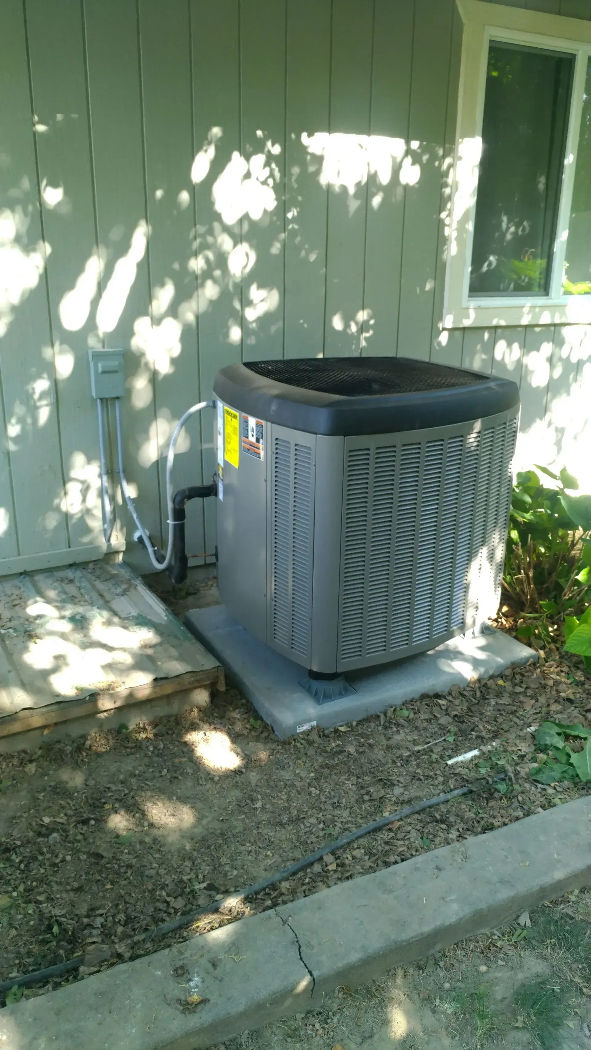 Air conditioning unit outside a house, grey with black top, set on concrete pad.
