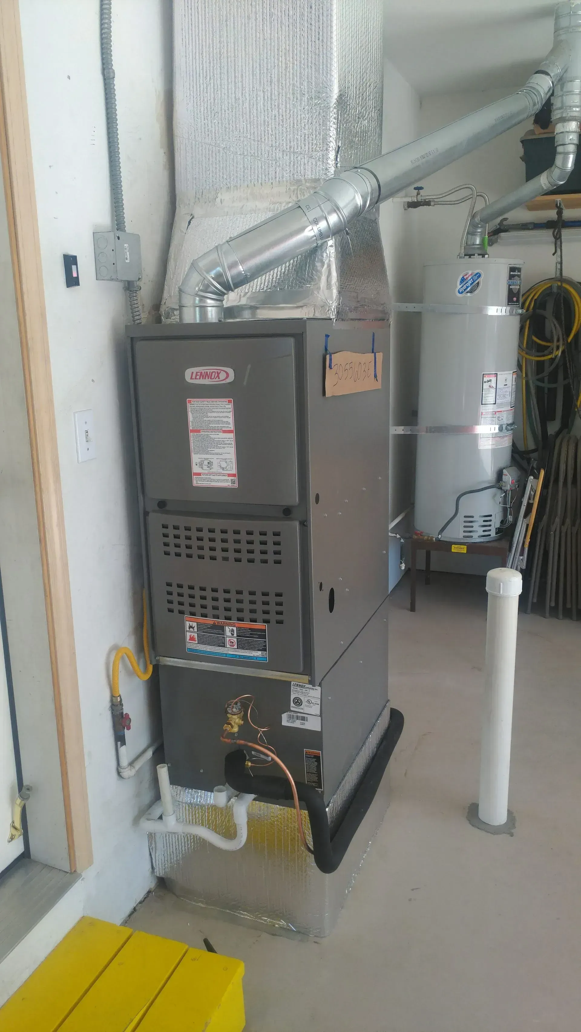 Furnace and water heater in a garage. Gray Lennox furnace with ductwork attached, white water heater to the right.