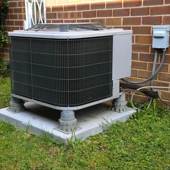 Central air conditioner unit on concrete base next to a brick wall.