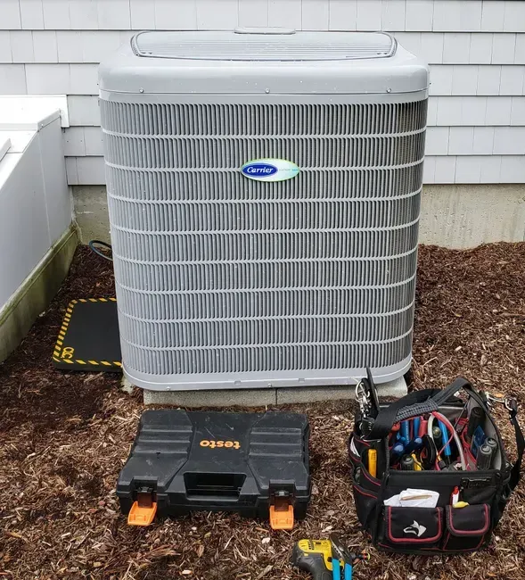 An air conditioning unit with tools; brown mulch ground.