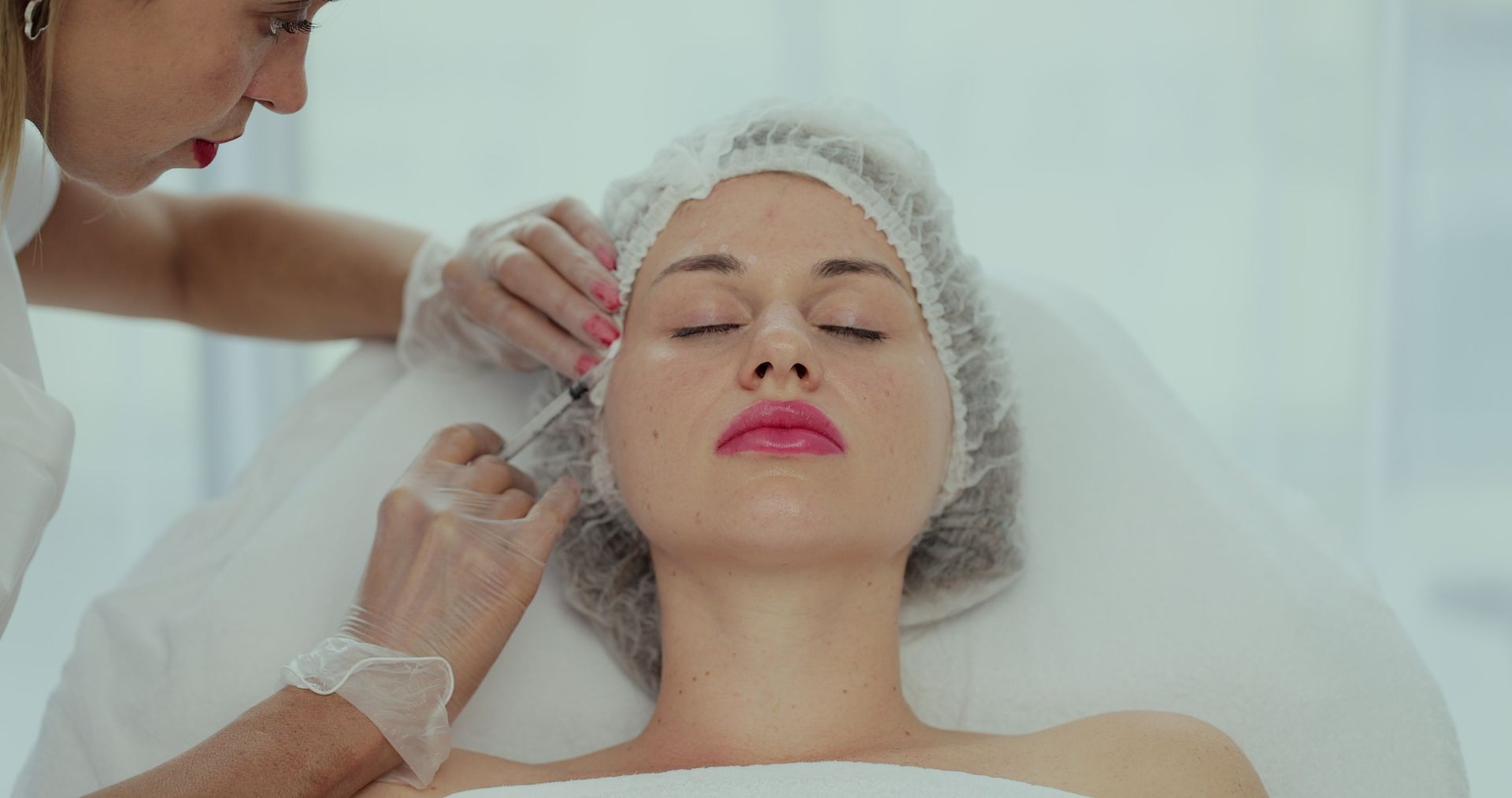Person receiving facial injection from a medical professional. Both are in a sterile setting.