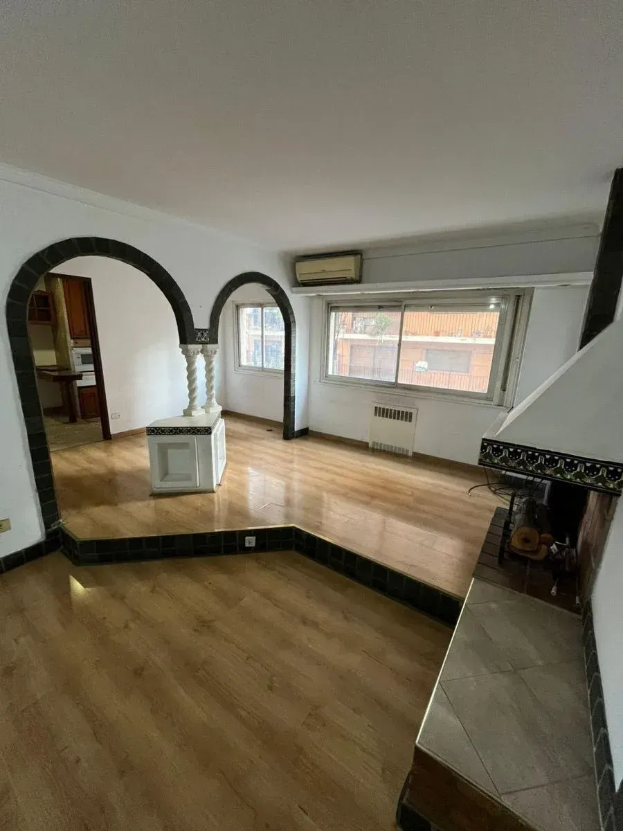 Sala de estar vacía con suelo de madera, espejo arqueado, banco junto a la ventana y chimenea de azulejos.