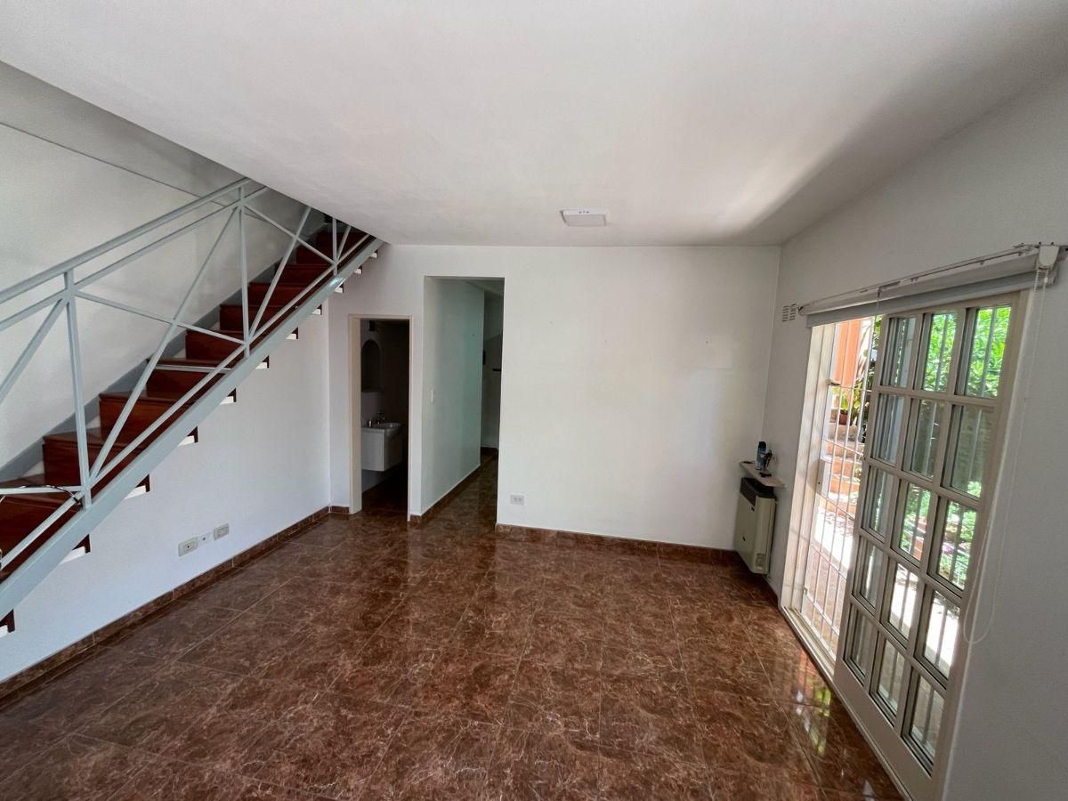 Sala de estar vacía con suelo de baldosas, escalera, puerta abierta y grandes puertas de cristal a la derecha.
