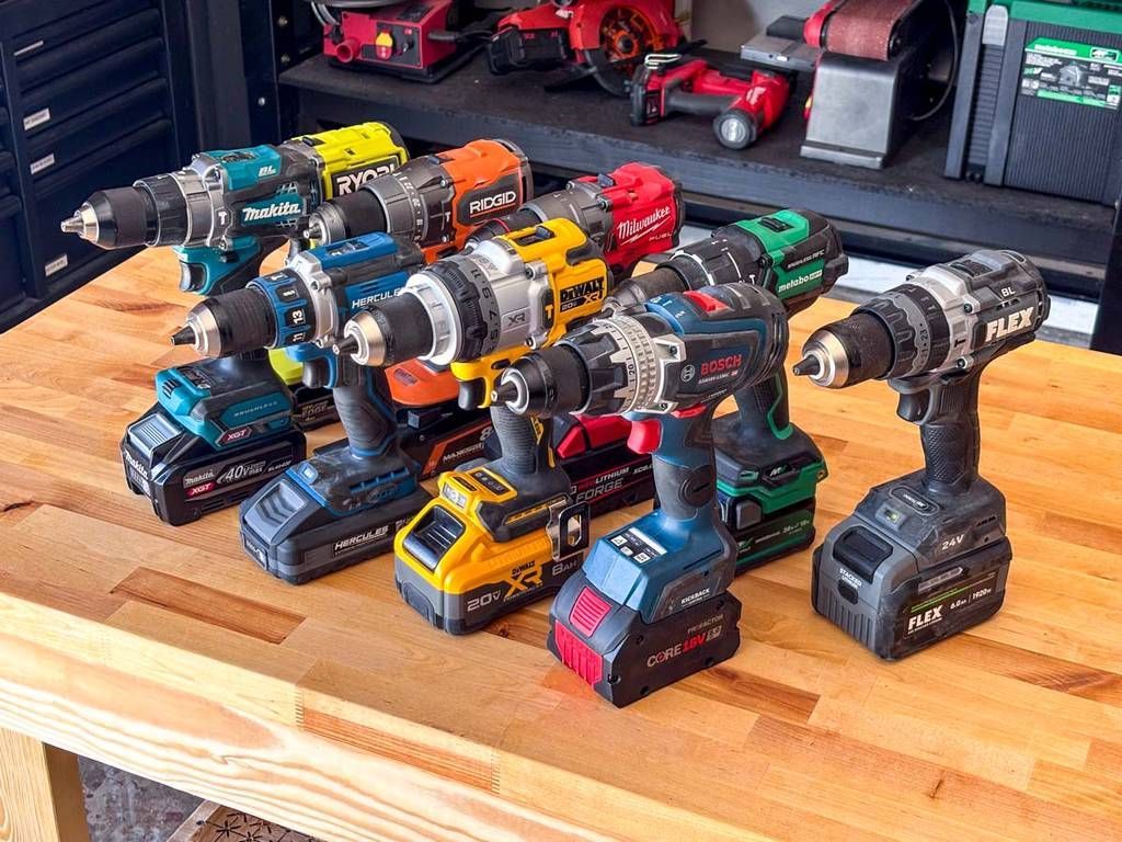 Assorted cordless power drills in various colors arranged on a wooden workbench.