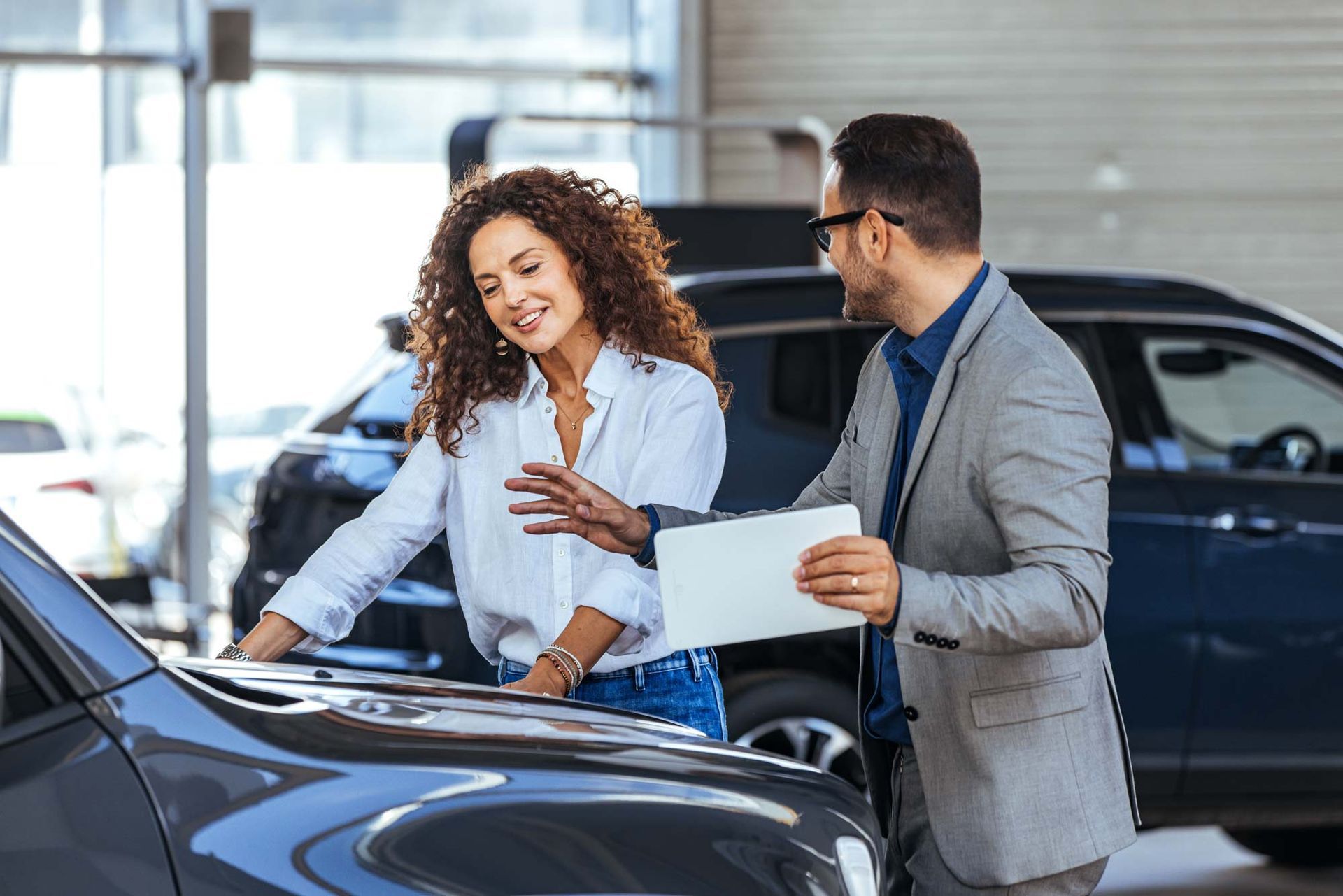 A man and a woman are looking at a car in a showroom. A man and a woman are looking at a car in a showroom.