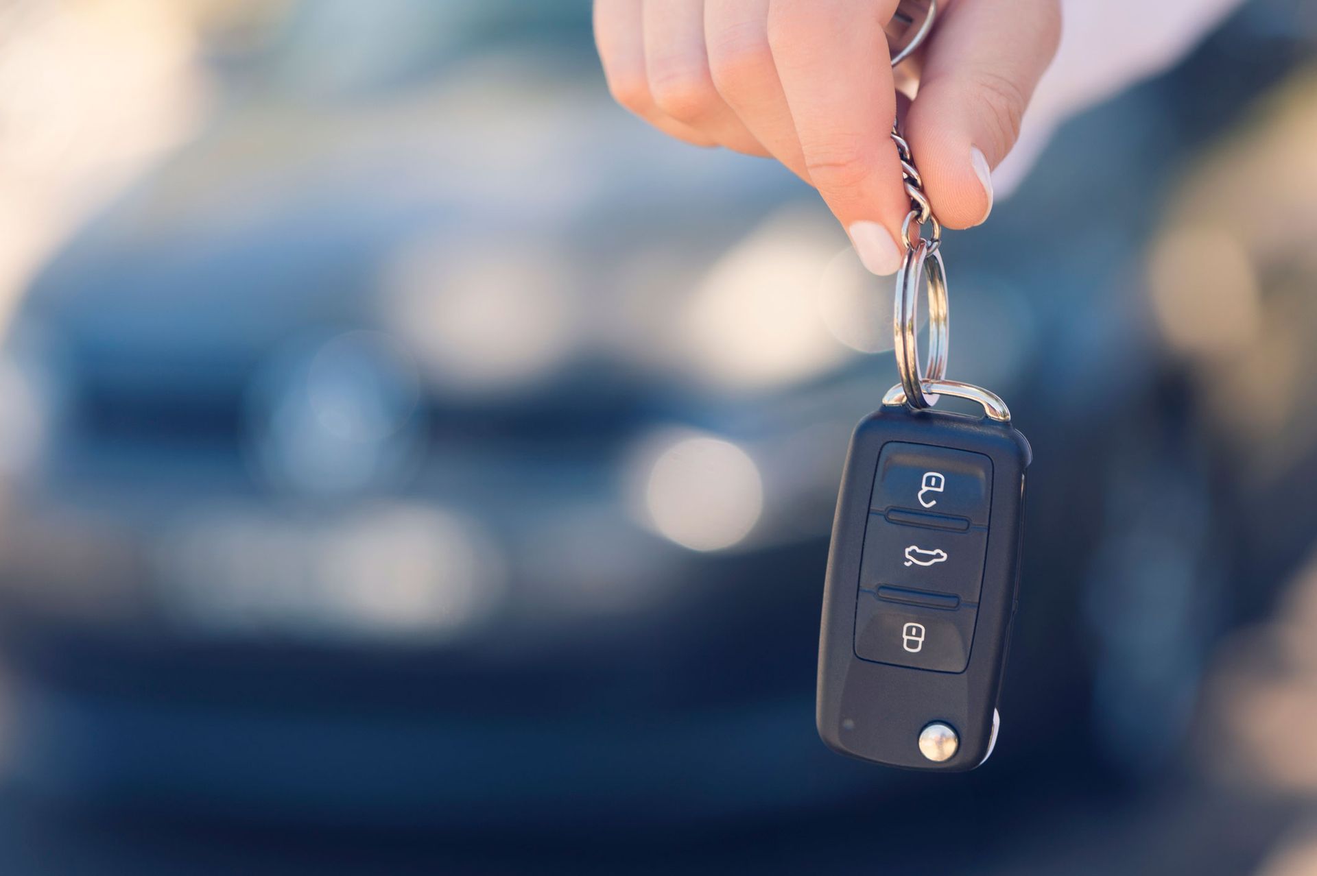 A person is holding a car key in front of a car. A person is holding a car key in front of a car.