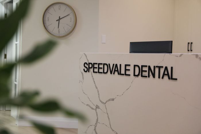 A clock is hanging on the wall above a speedvale dental reception desk.