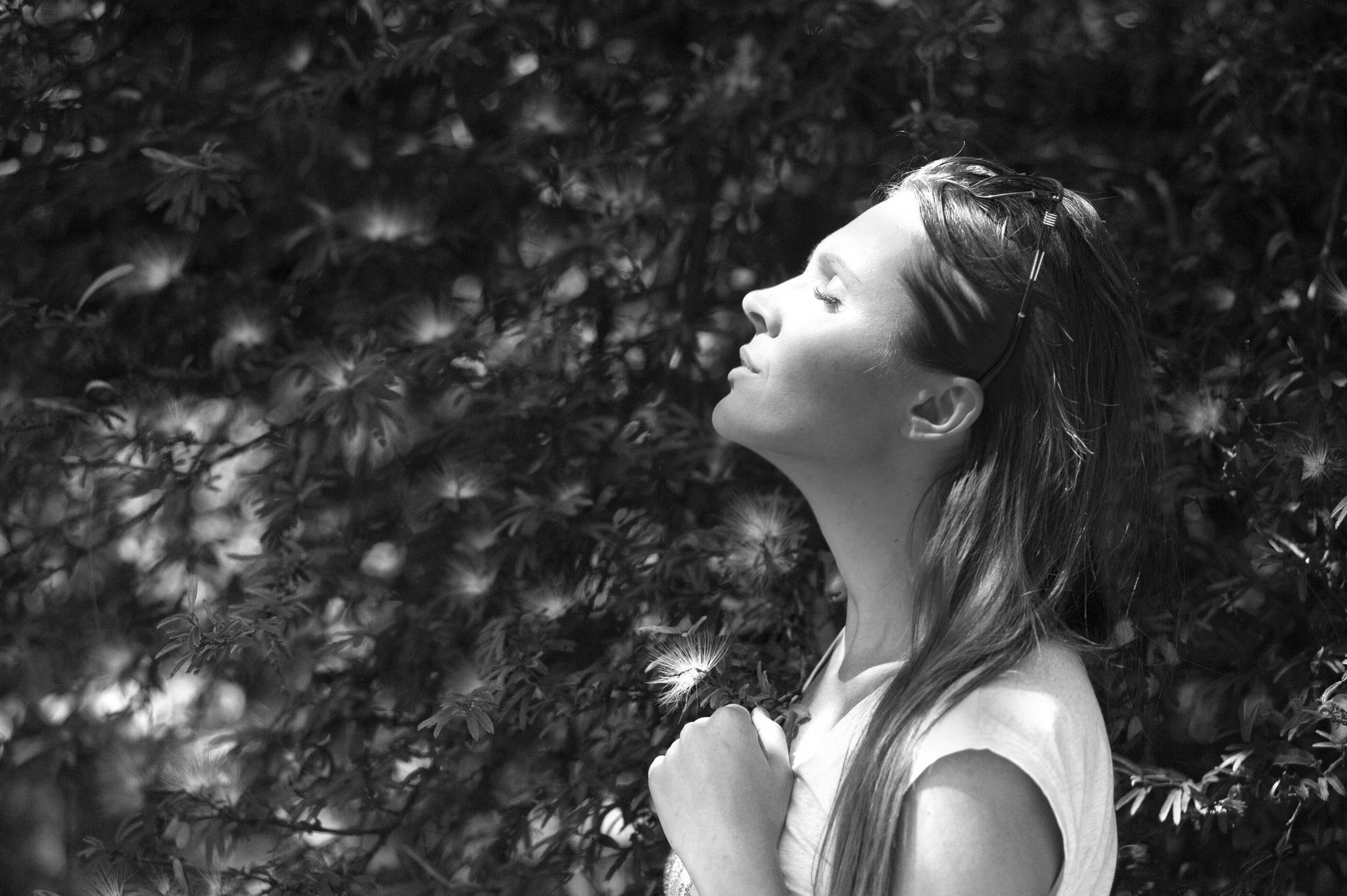A woman is standing in front of a tree with her eyes closed.