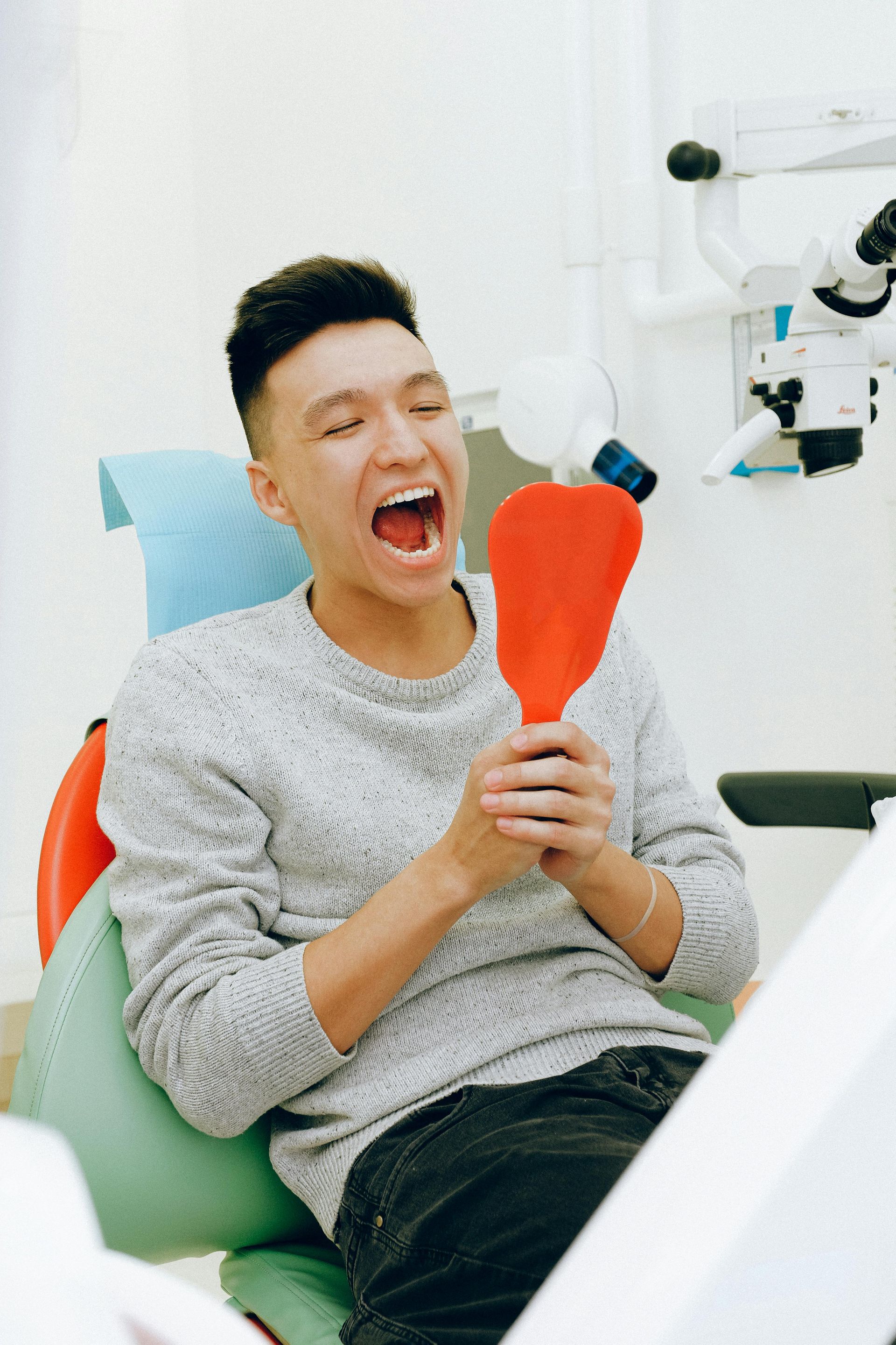 A man is sitting in a dental chair looking at his teeth in a mirror.