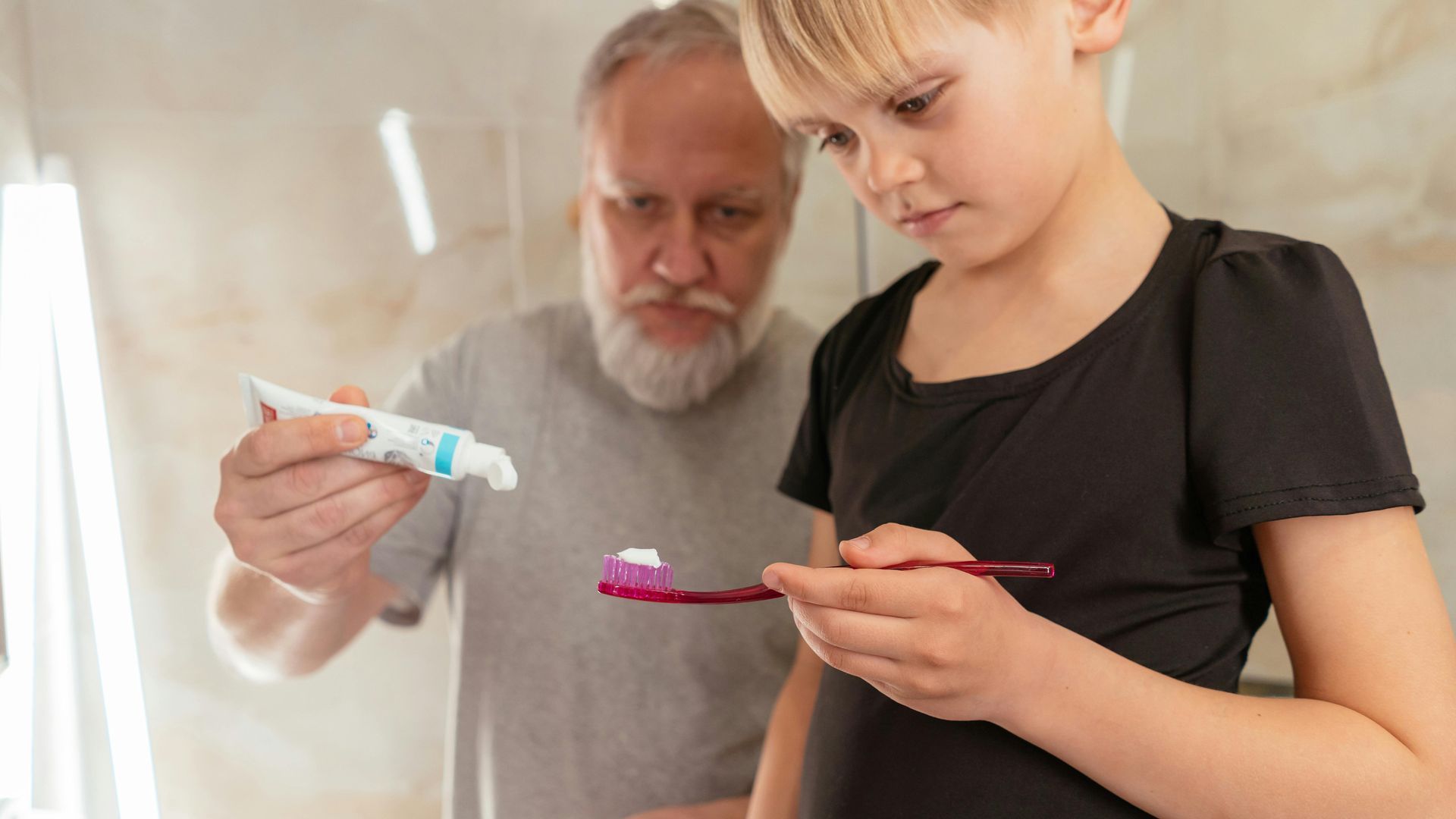 An elderly man is teaching a young girl how to brush her teeth.