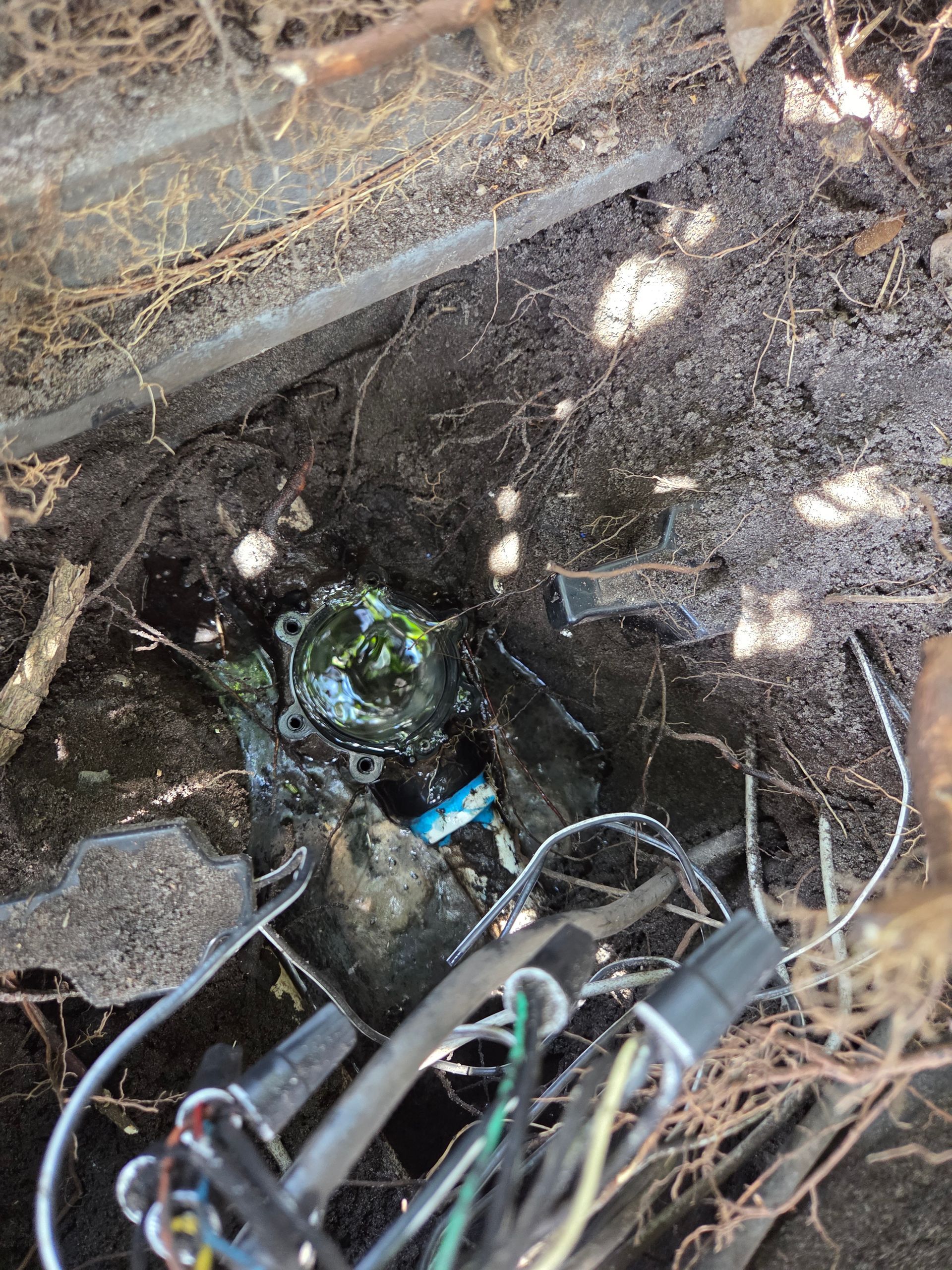 Close-up of a damaged, buried utility box, wires, and soil, with a partially exposed, corroded component.