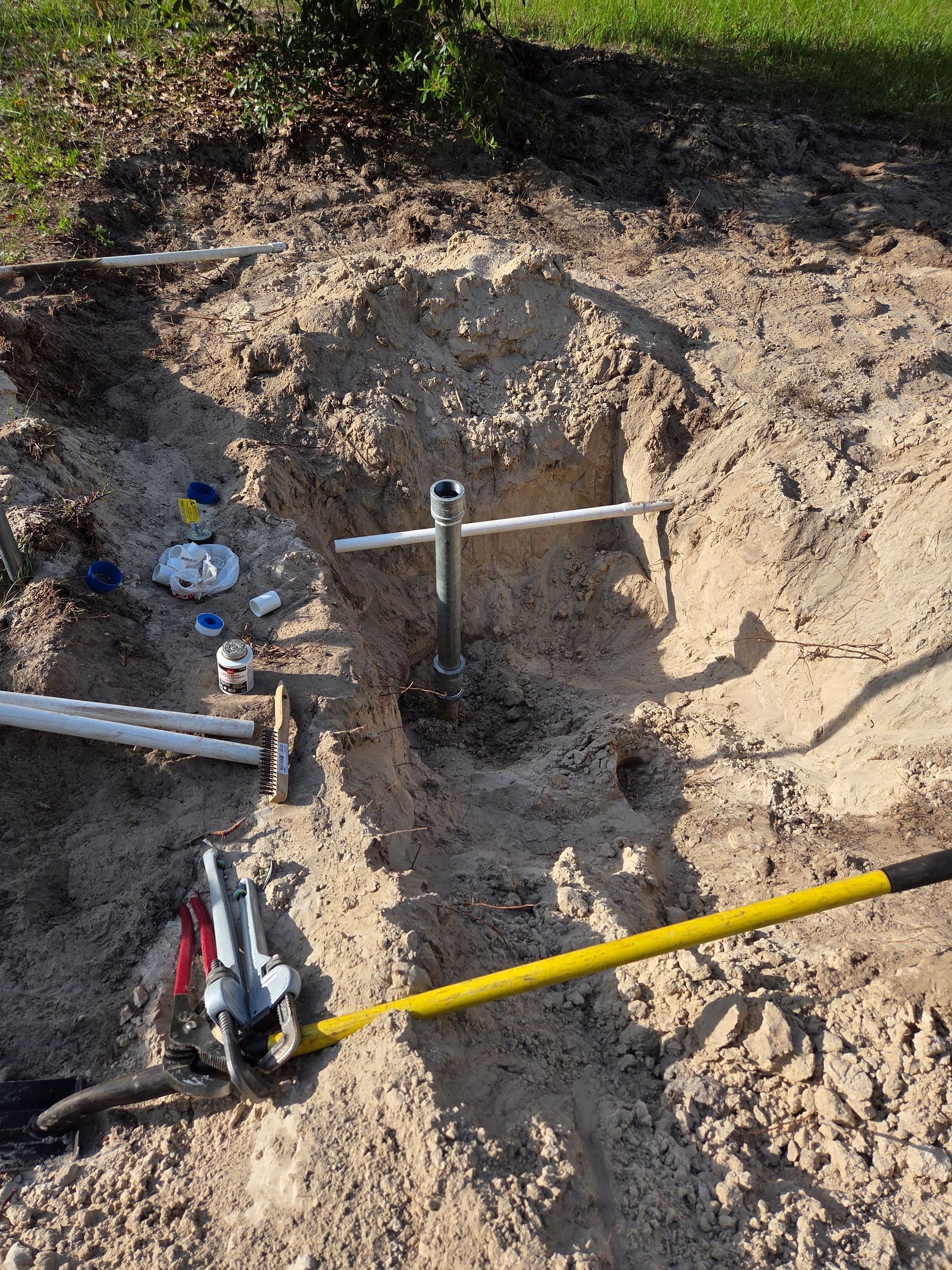 A well installation site with PVC pipes, tools, and a central pipe in a dug hole.