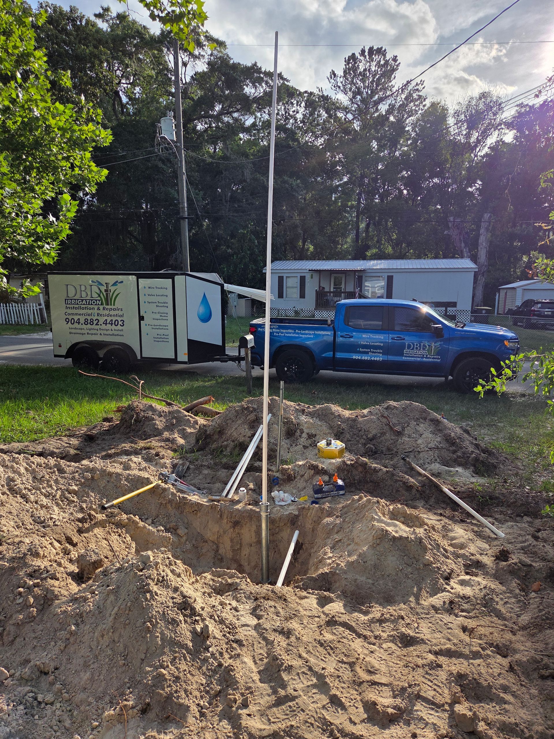 Well drilling site: A tall metal pole extends from a hole in the ground. A blue truck and trailer are nearby.
