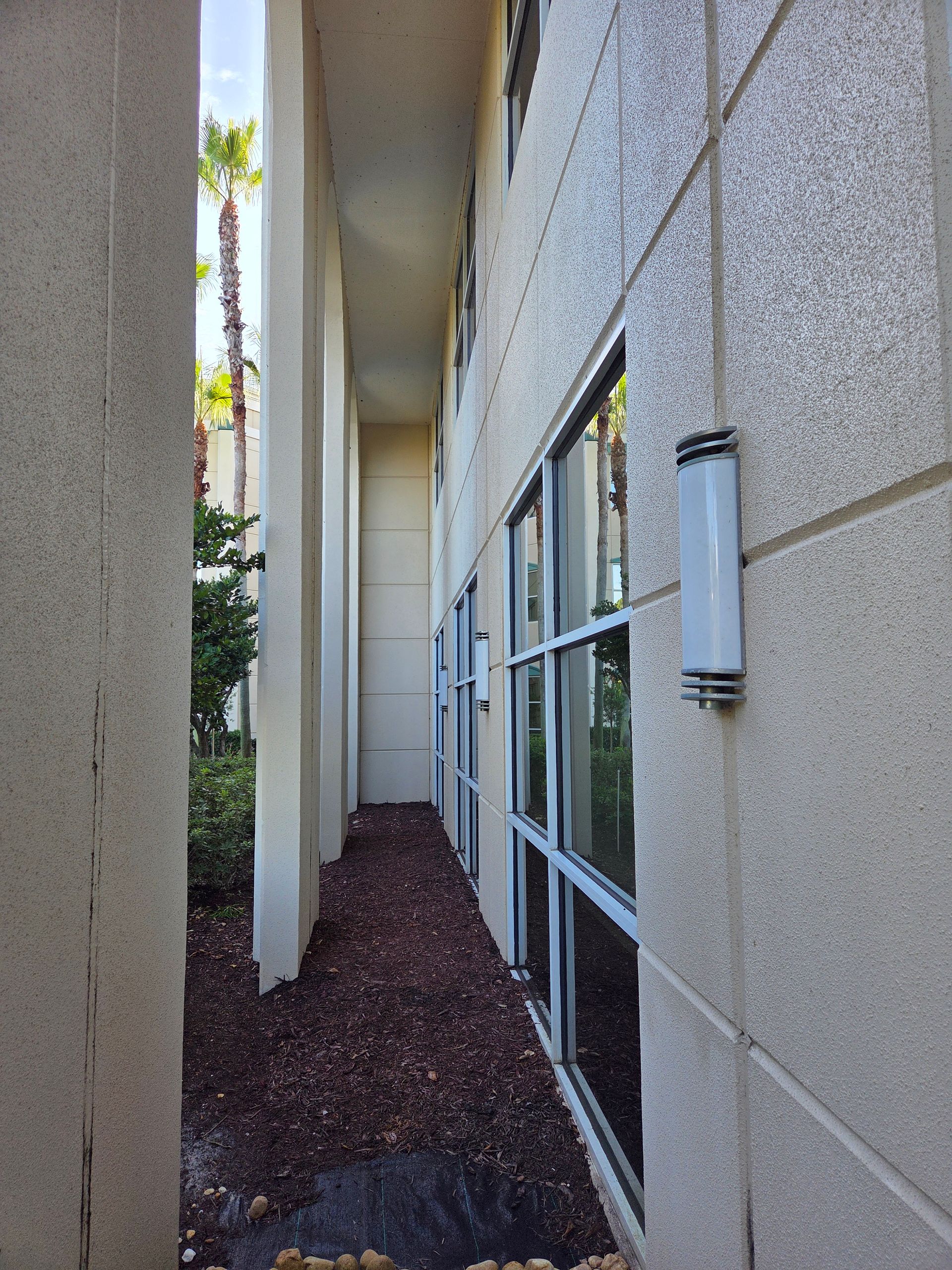 Exterior building with windows, columns, and a narrow walkway with dark brown mulch.