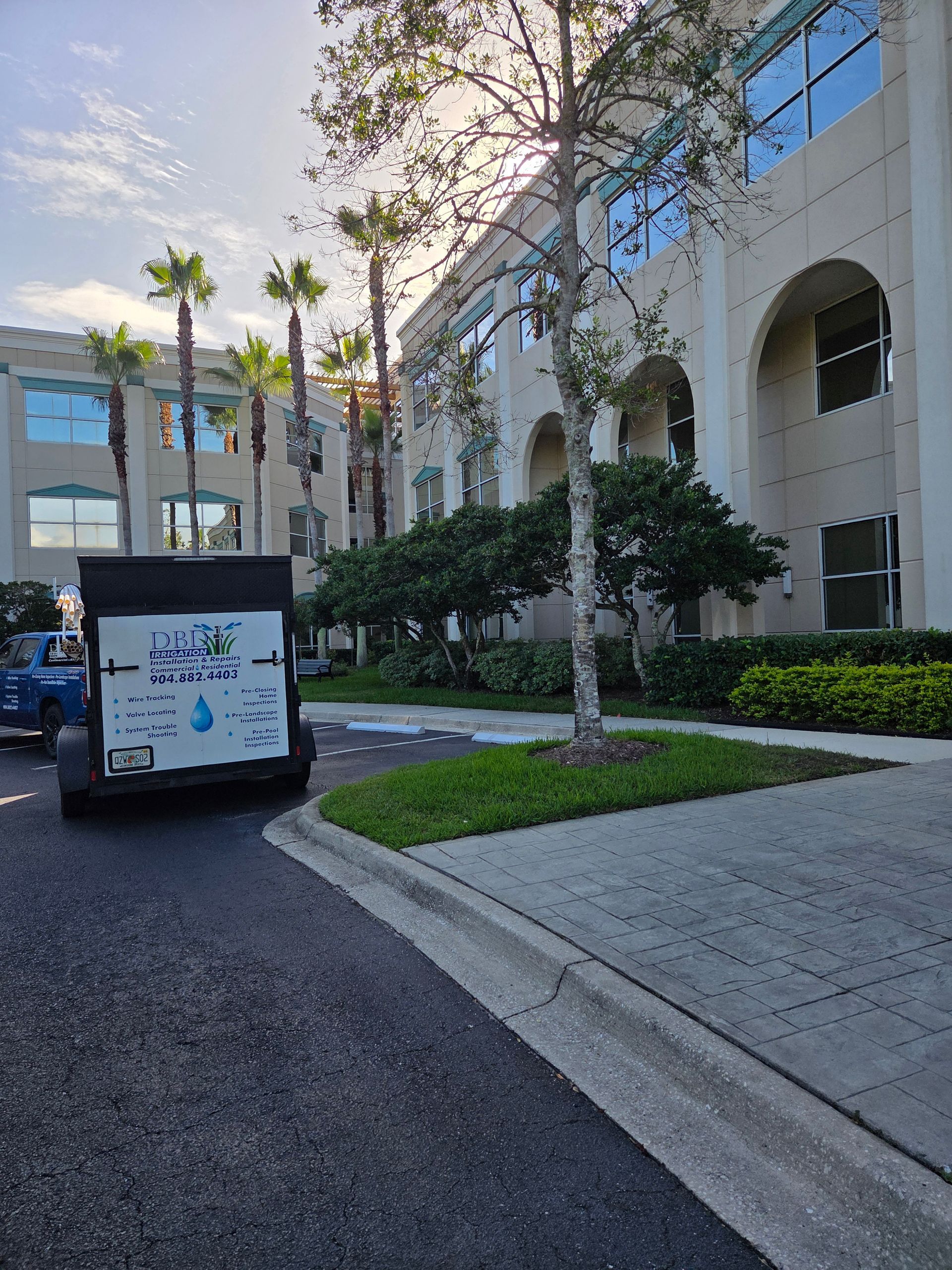Service truck parked in front of a light-colored building with arched windows and palm trees. Sunny outdoor setting.