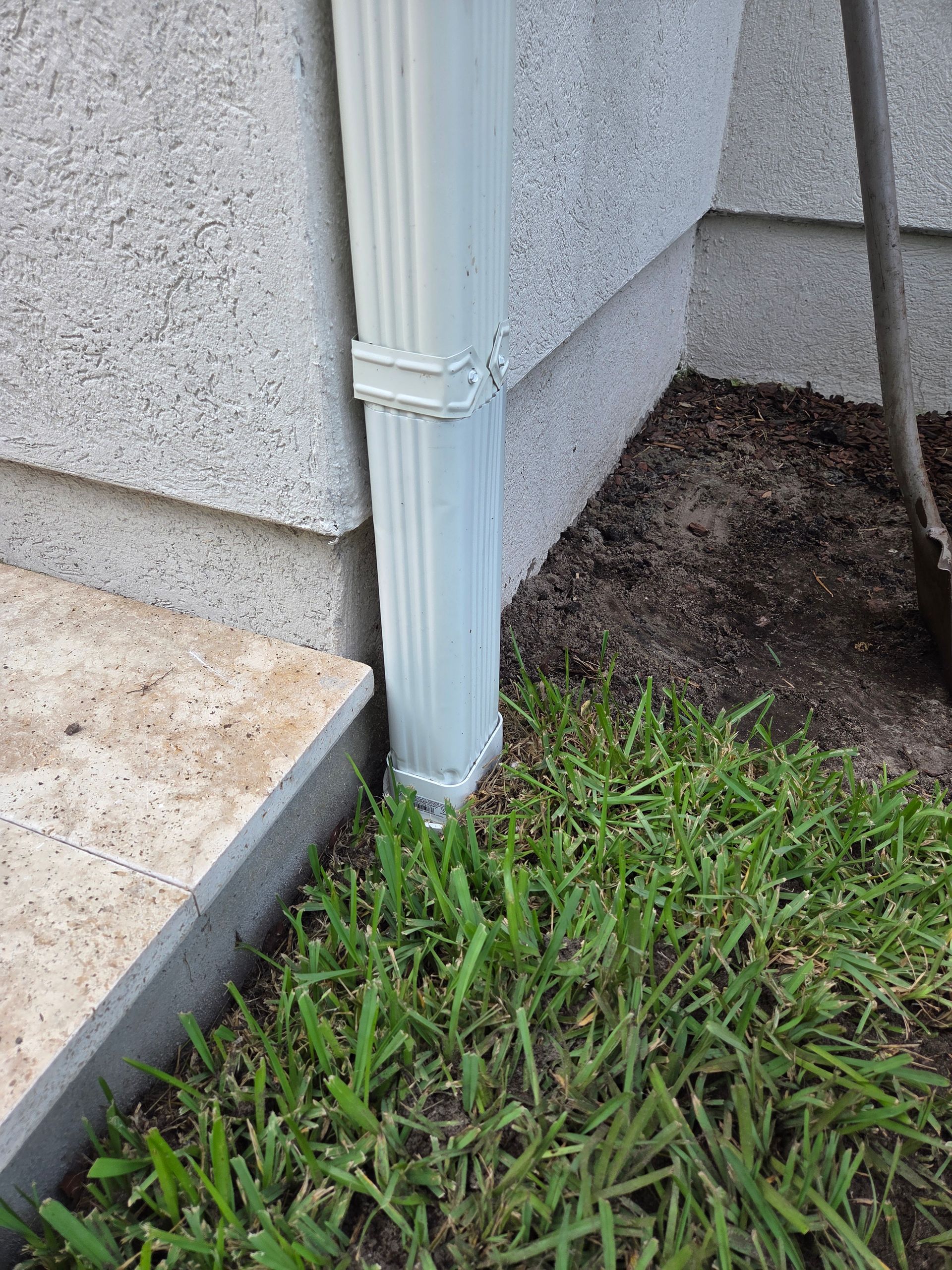 Gray downspout next to a concrete wall and grass.