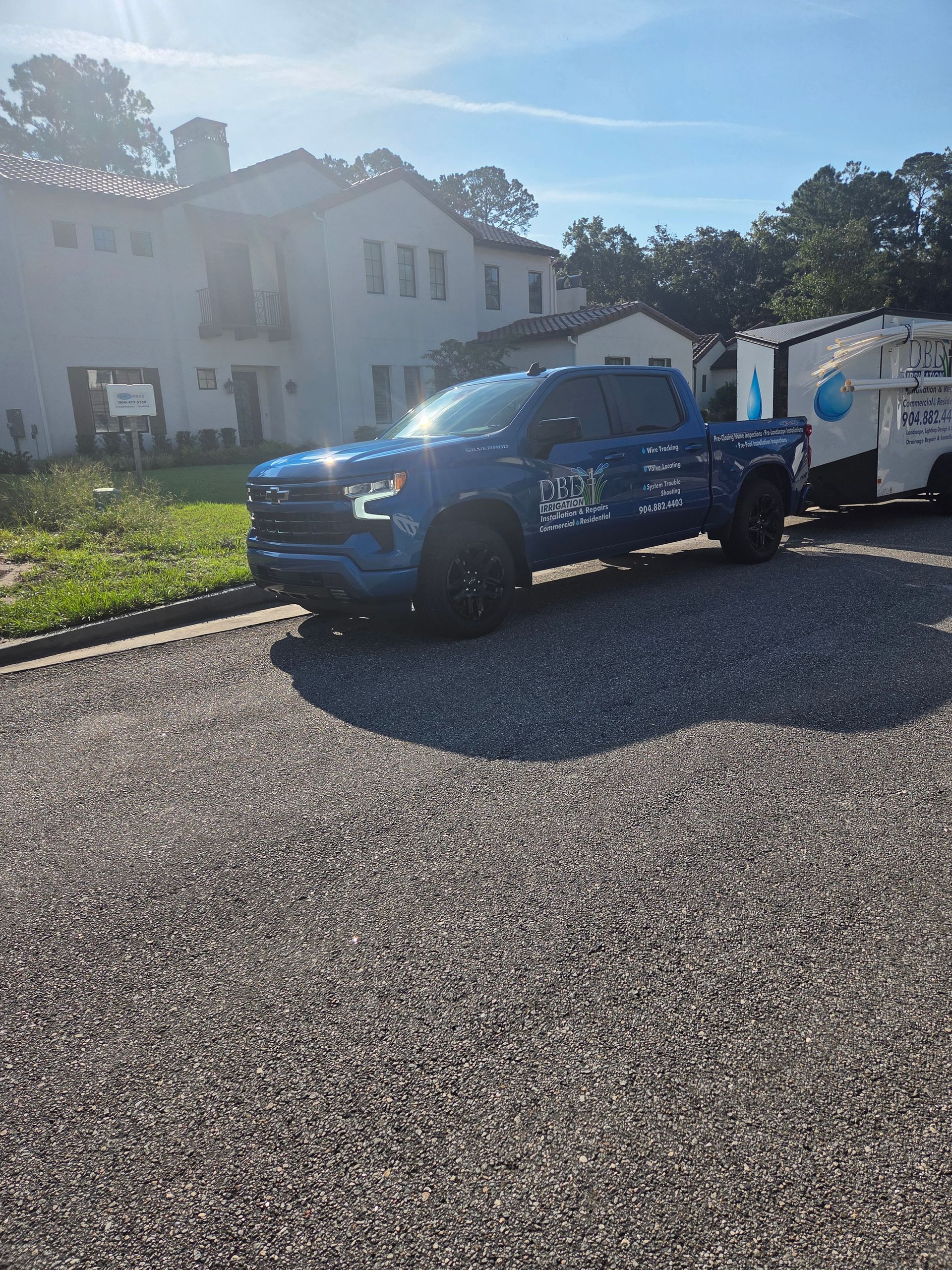 Blue pickup truck parked in front of a white building with a trailer. Sunny day.