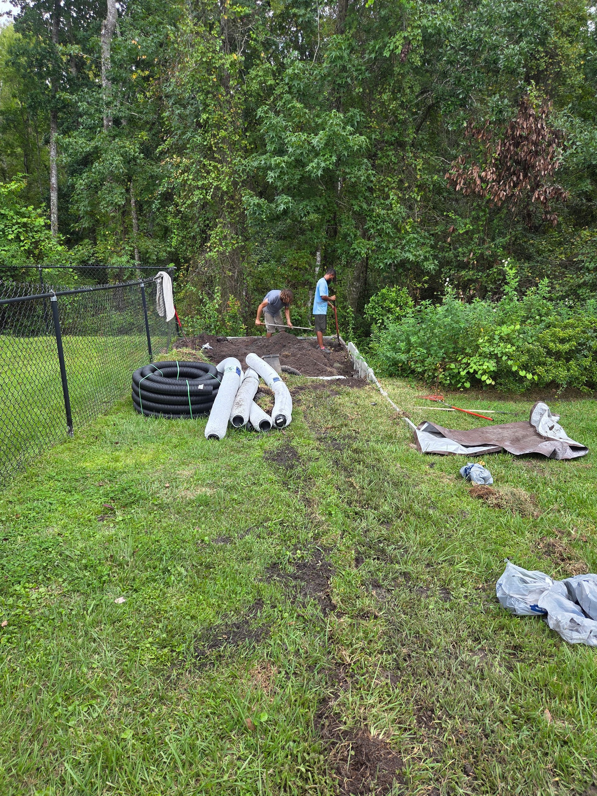 People working in a garden bed, surrounded by grass and trees.