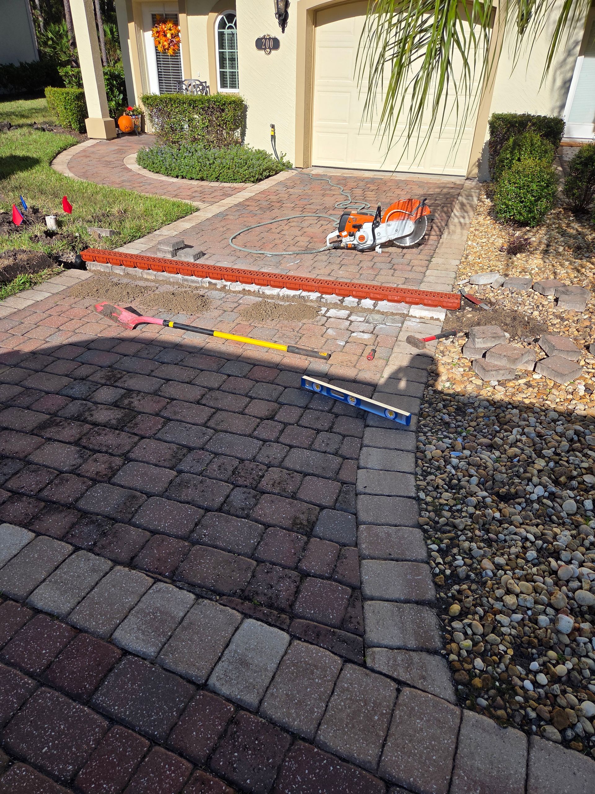 Brick driveway under construction, with tools and materials visible.