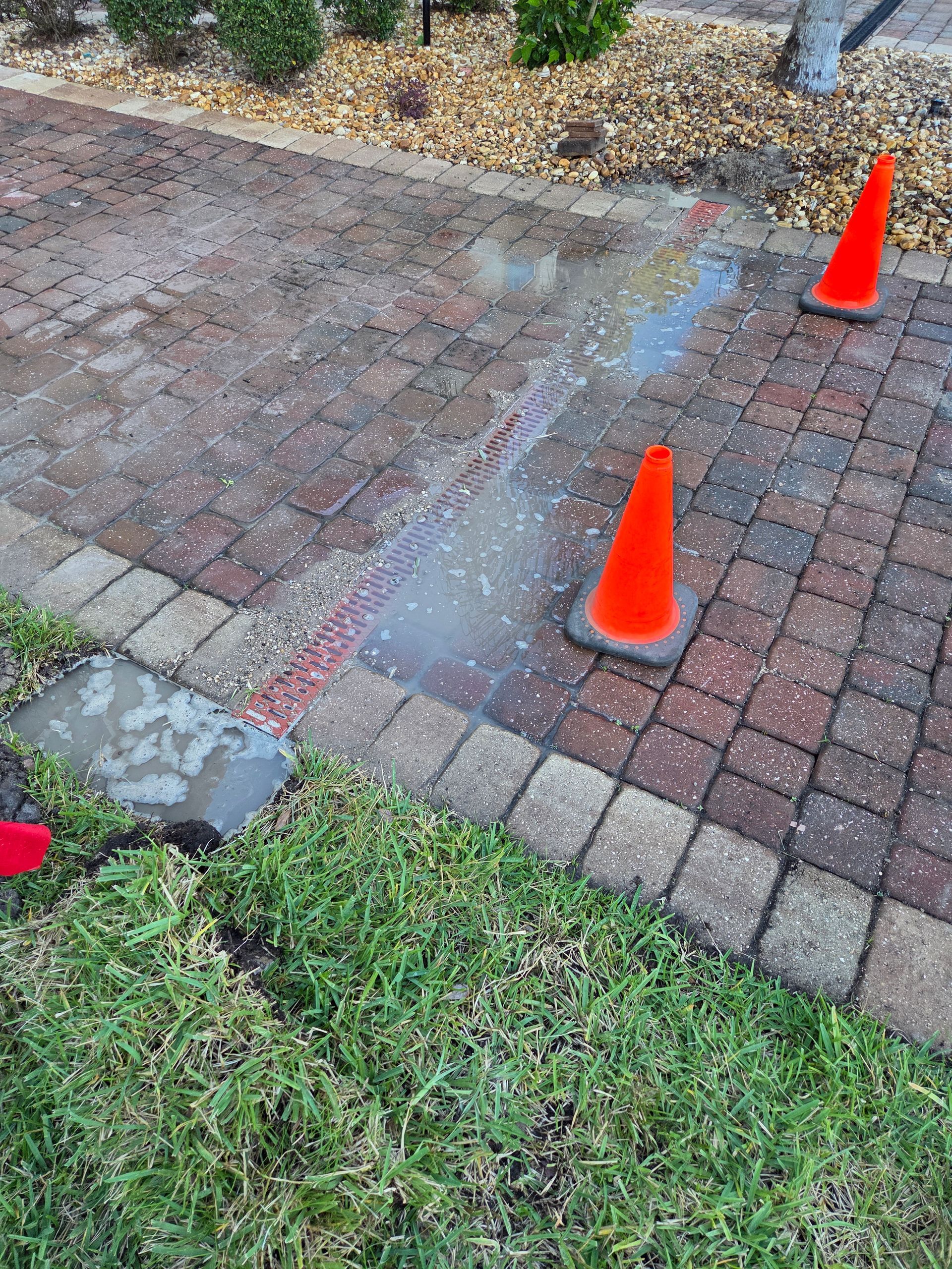 Water spraying from a damaged brick path, marked by orange cones.
