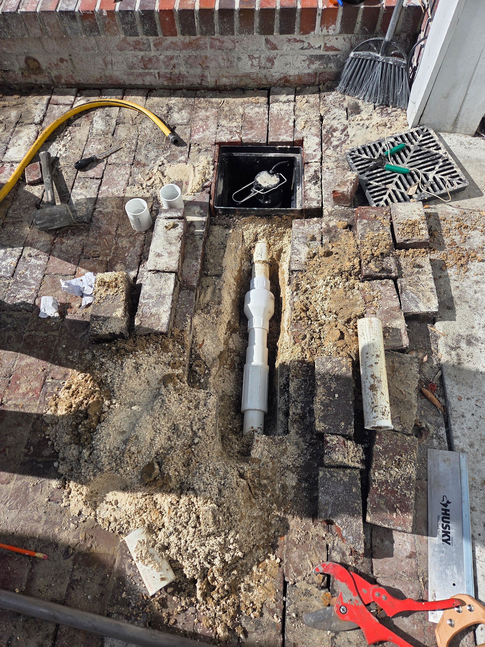 Construction site: bricks removed, exposing plumbing, sawdust, and tools on a patio.