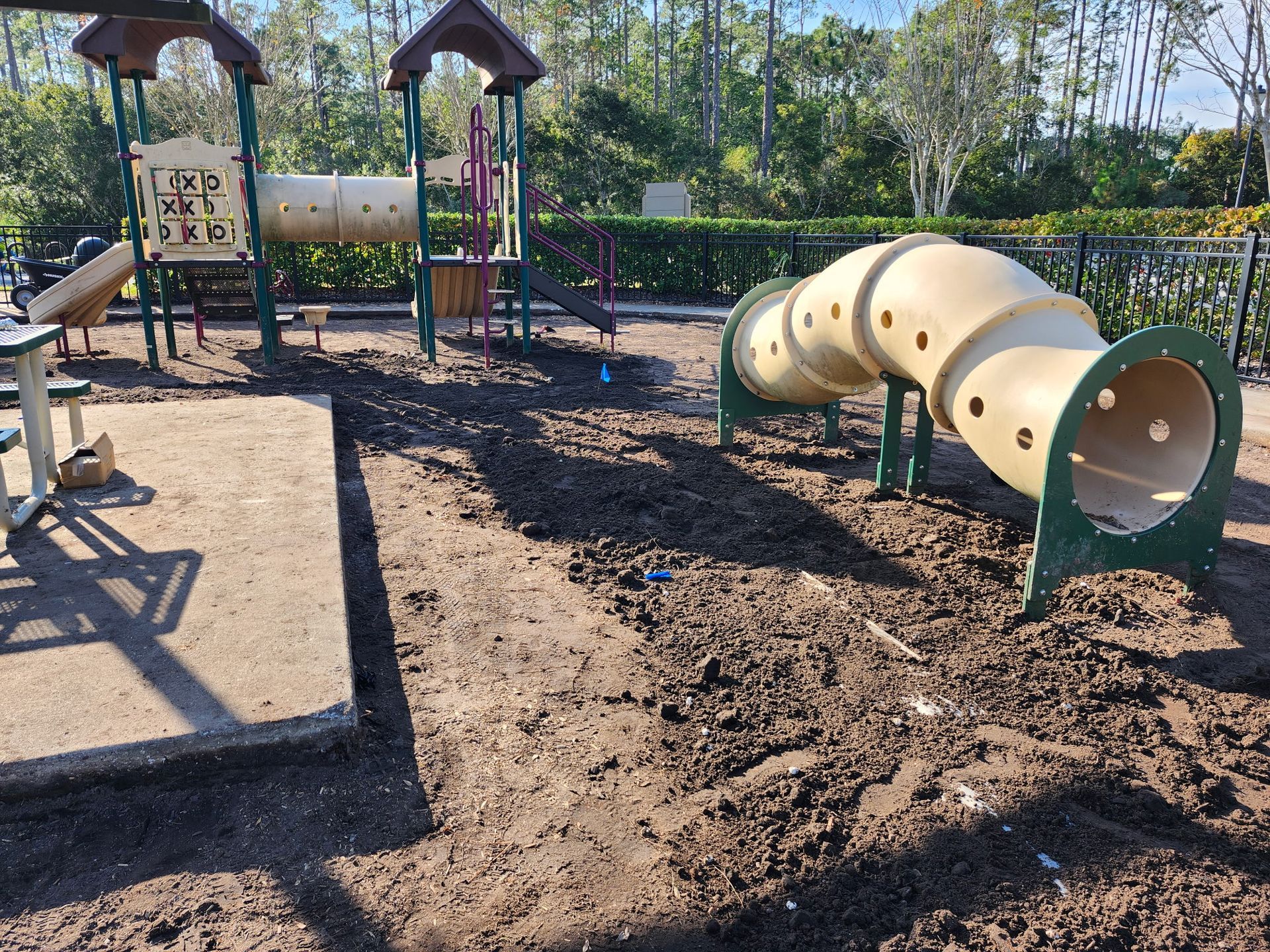 Playground with brown dirt ground, beige tunnel slide, and various play structures.