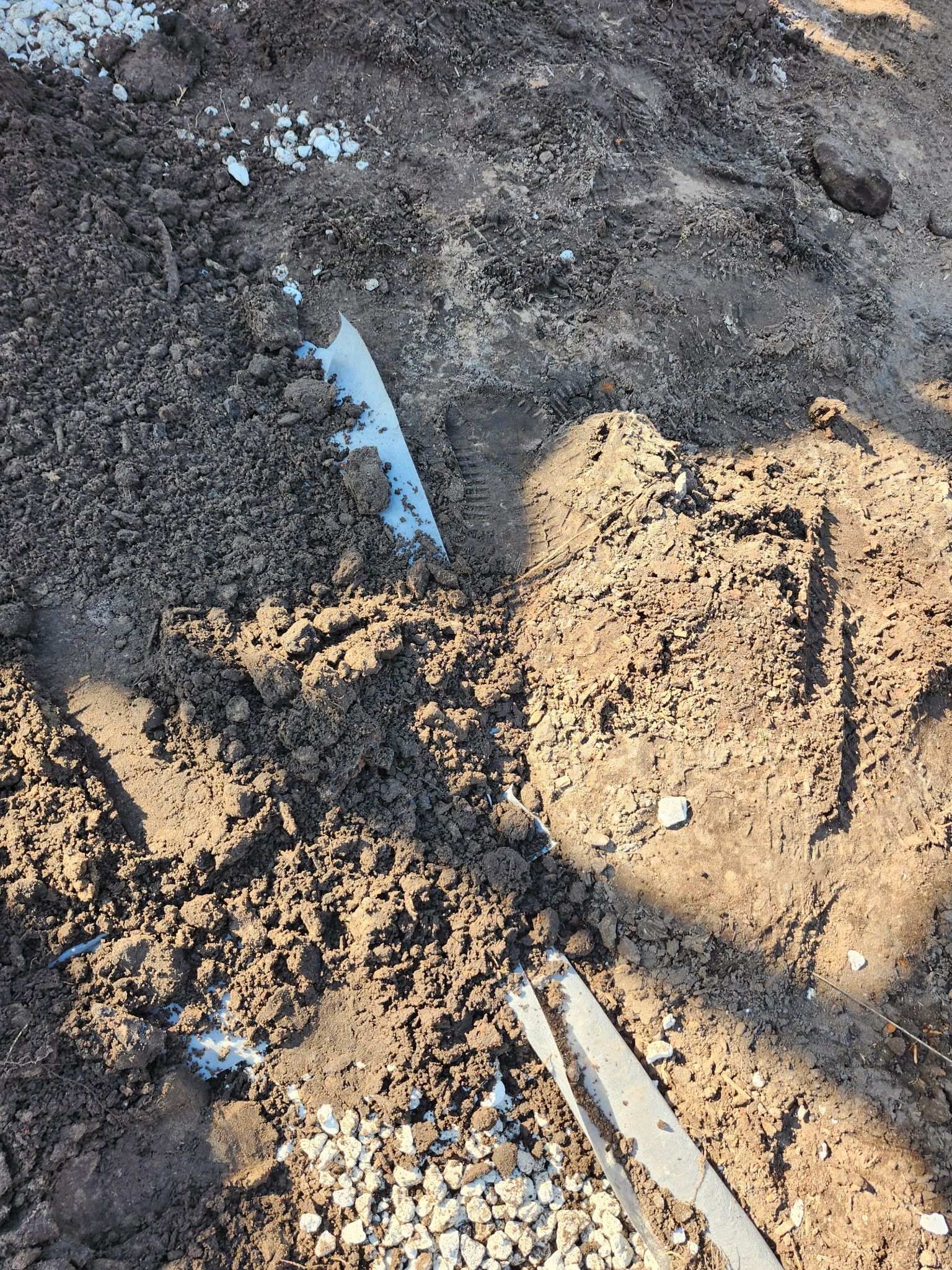 Dirt pile with a partially buried white and grey strip, possibly concrete.