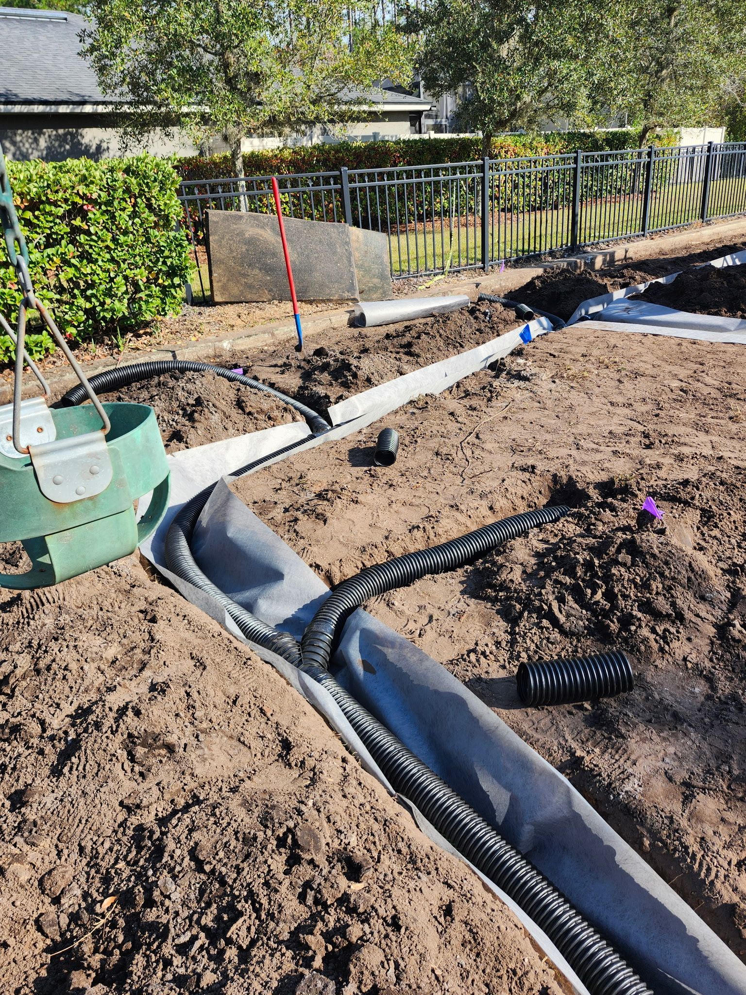 Trench drain installation in a yard with black corrugated pipe wrapped in fabric, and a fence.
