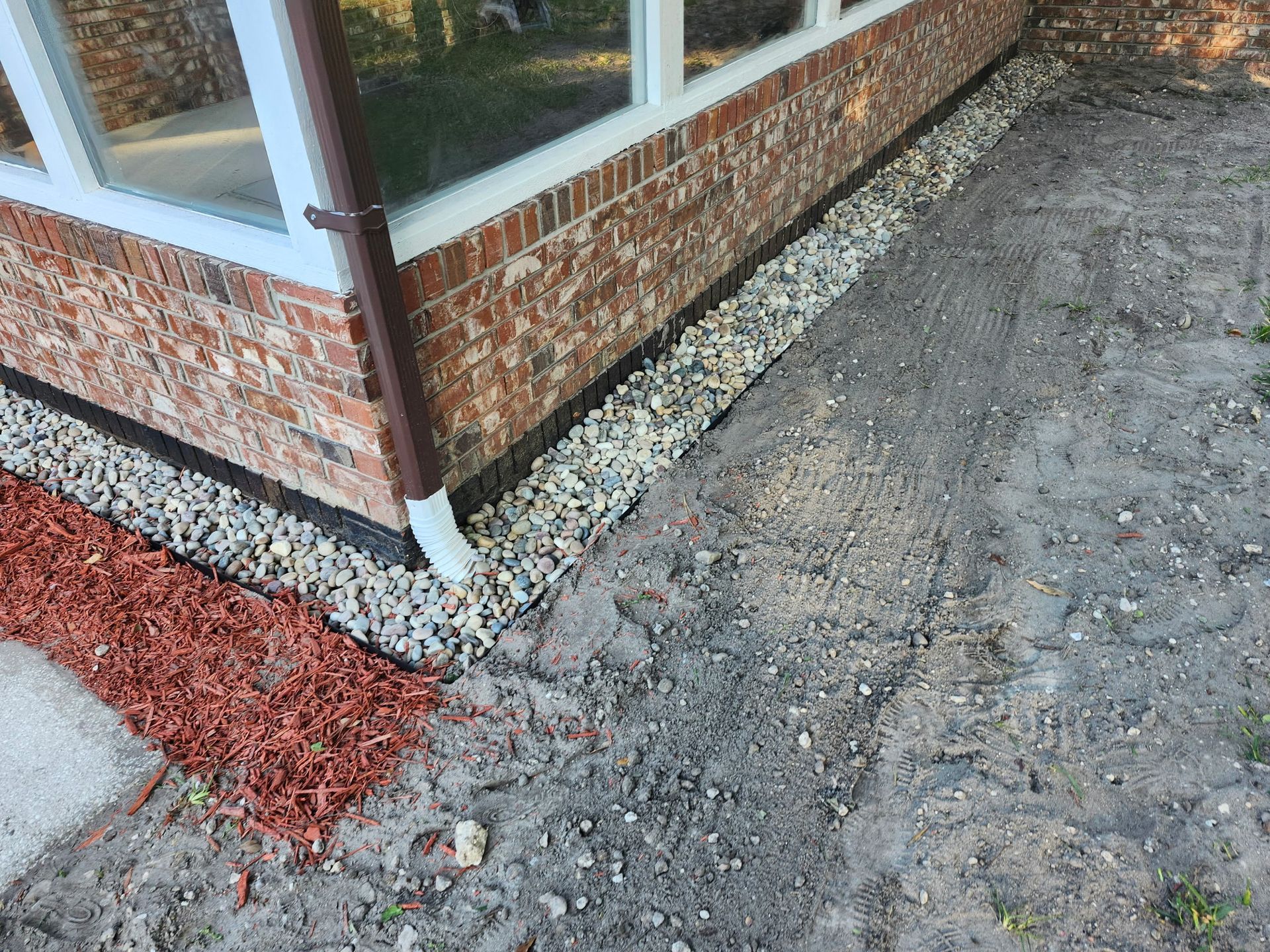 Exterior of building with brick facade, gravel border, and muddy ground. Red mulch to the left.