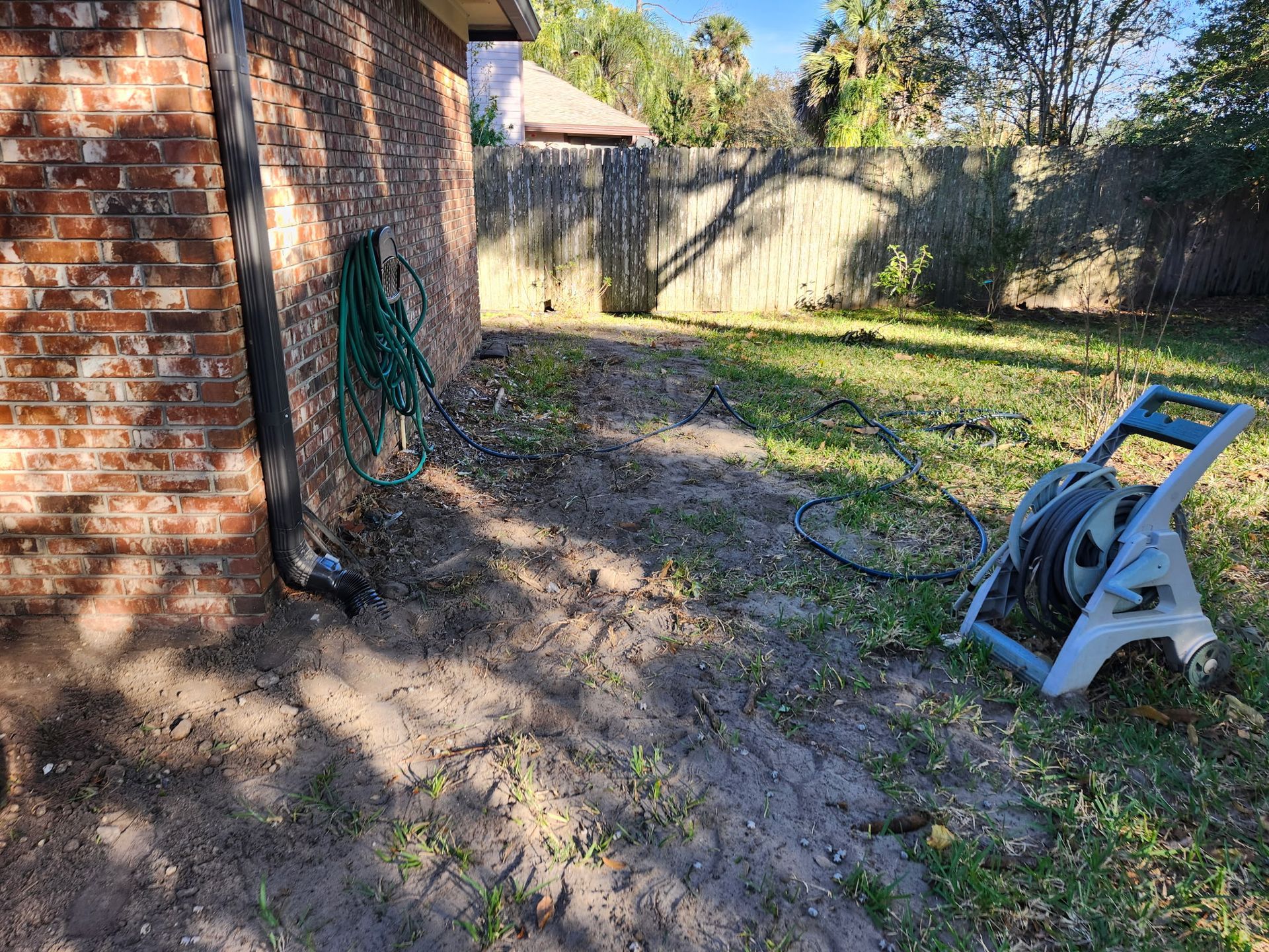 Brick building exterior with a muddy yard, hose reel, and wooden fence in the background.