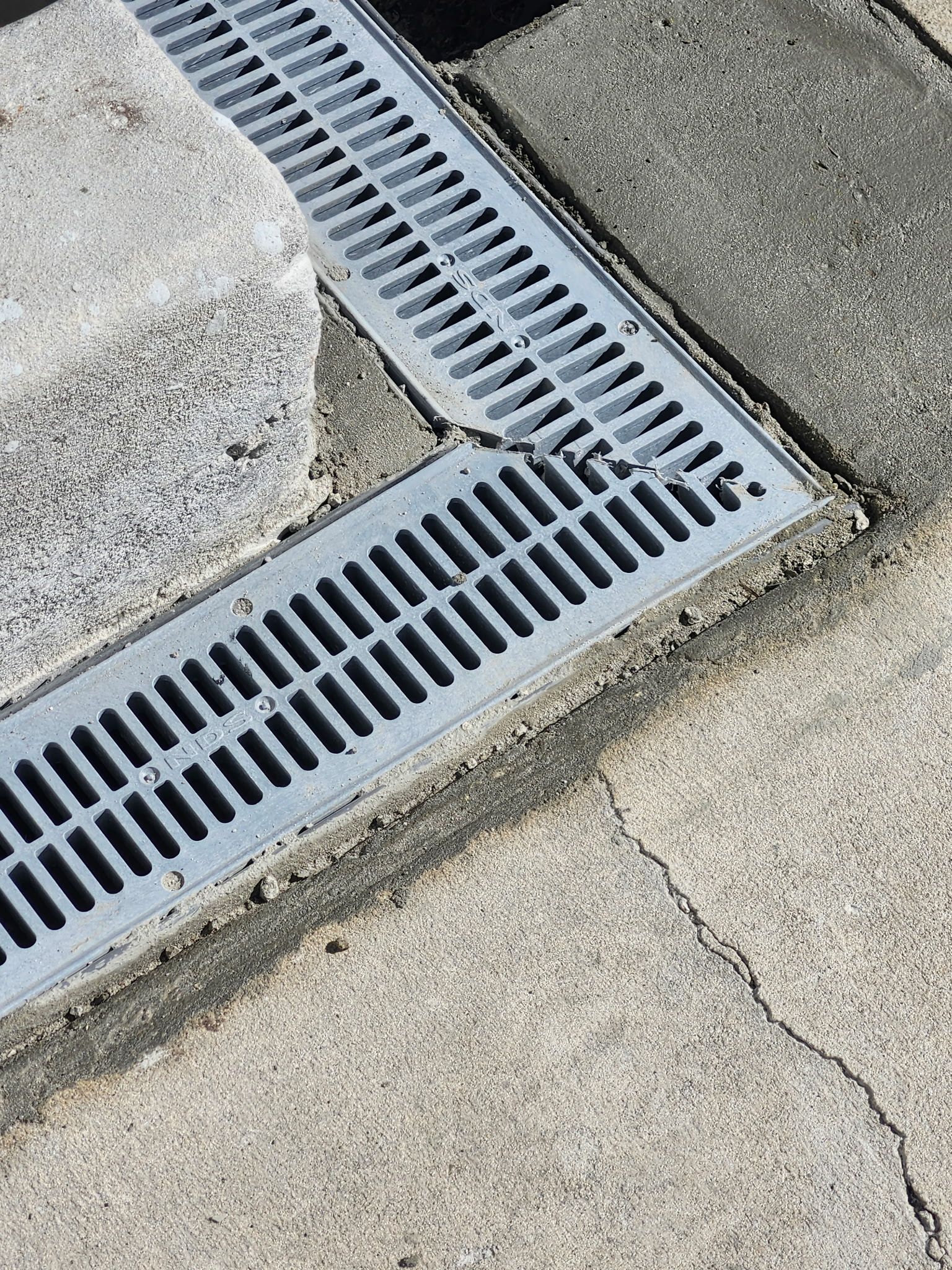 Metal grate drain in concrete next to a stone step.